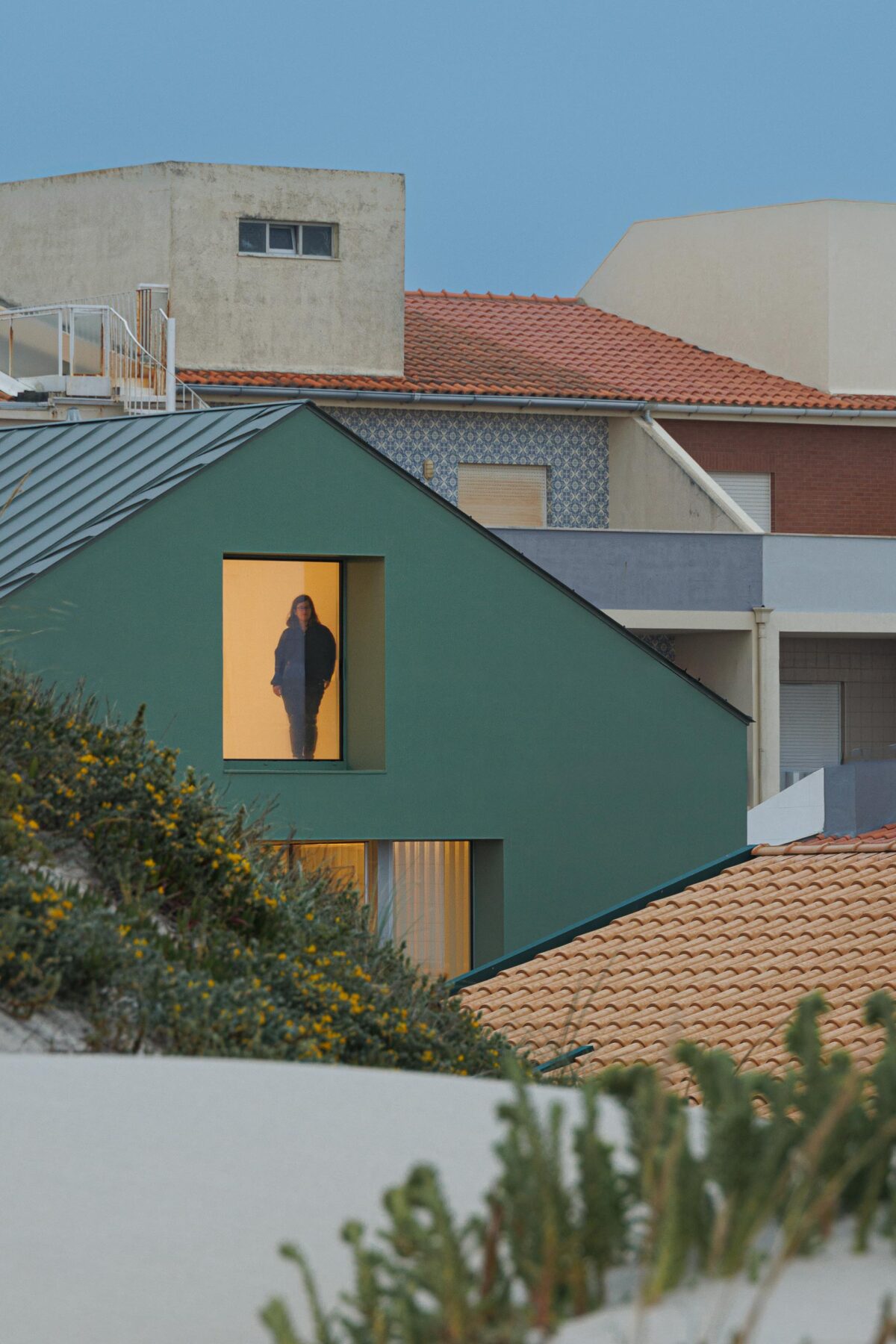 Vão da mansarda iluminado ao entardecer, revelando o interior da moradia e a presença humana — Casa Verde arquitectura M2 Senos Arquitectos fotografia Ivo Tavares