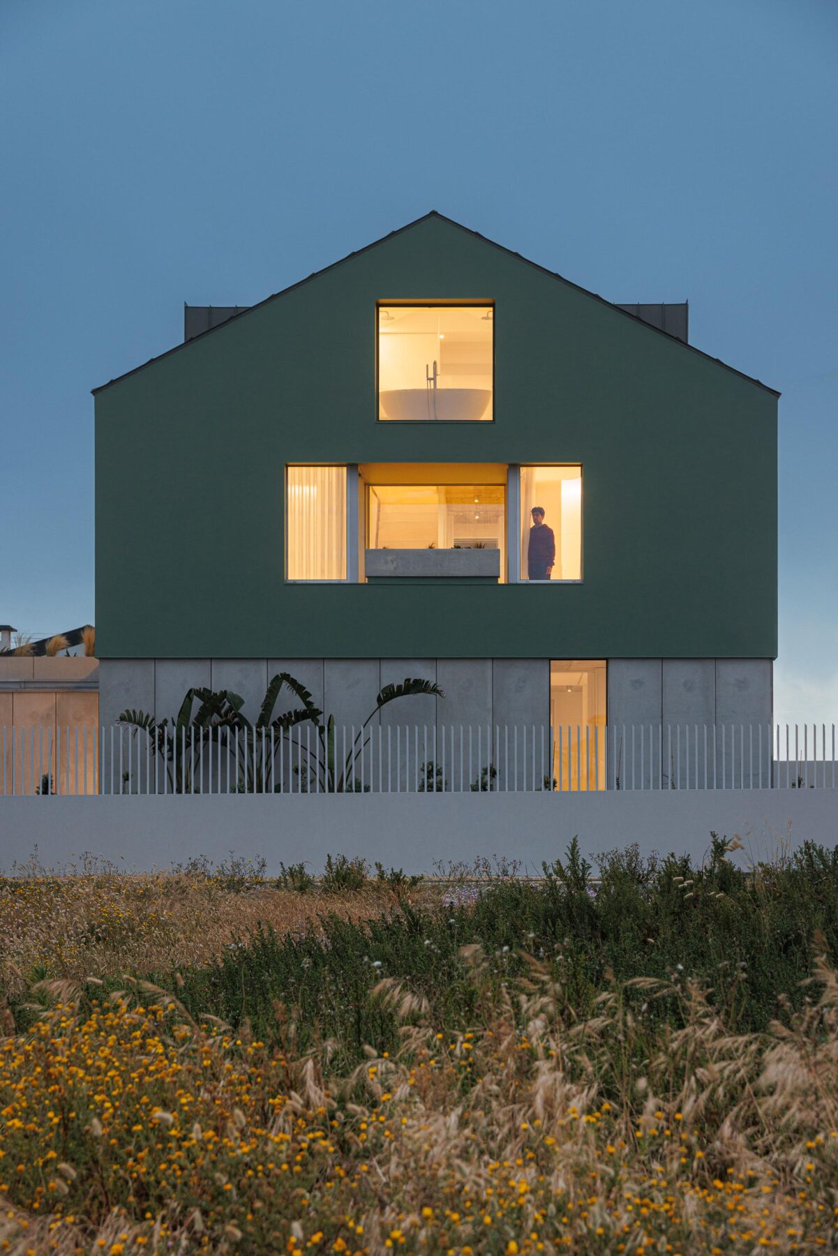 Fachada principal da moradia verde com embasamento em betão, vãos iluminados e cobertura inclinada, ao entardecer — Casa Verde arquitectura M2 Senos Arquitectos fotografia Ivo Tavares