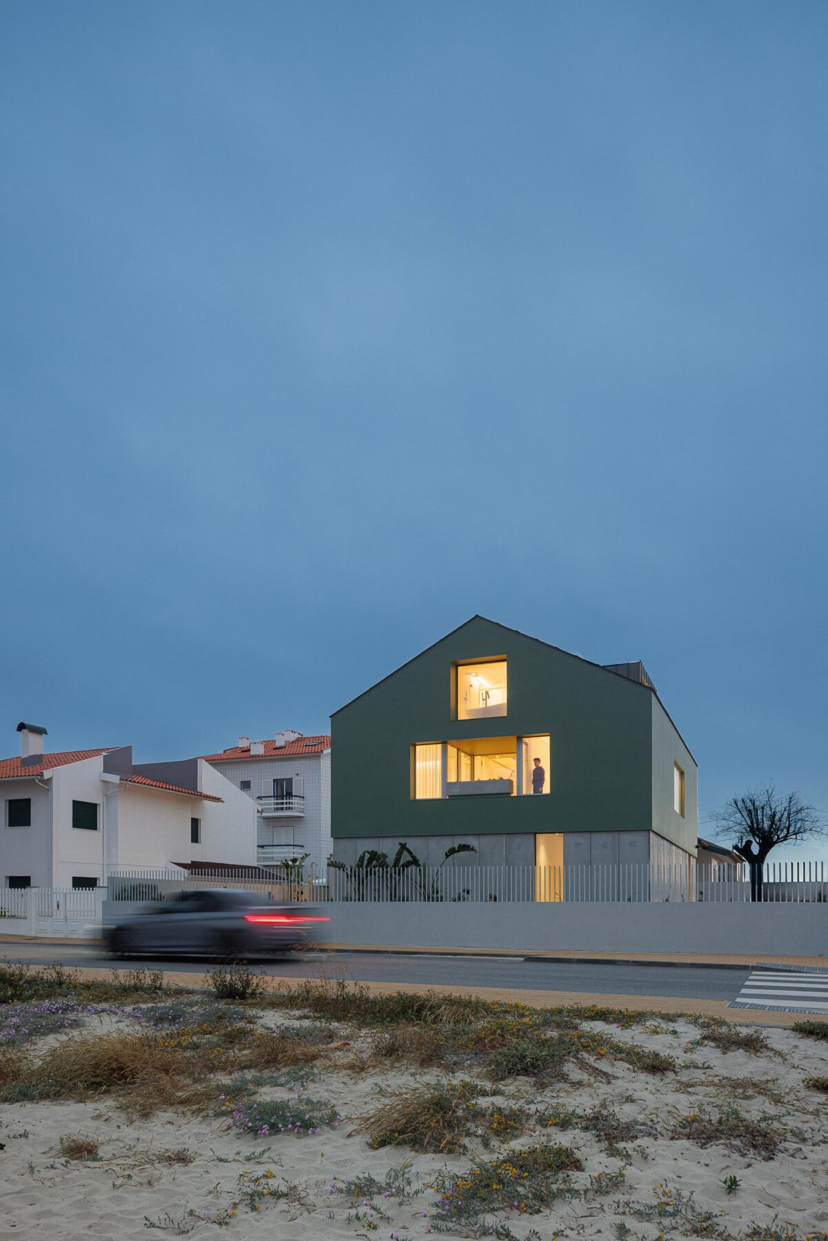 Moradia de volume compacto verde com cobertura inclinada e mansarda, iluminada ao entardecer, vista da rua — Casa Verde arquitectura M2 Senos Arquitectos fotografia Ivo Tavares