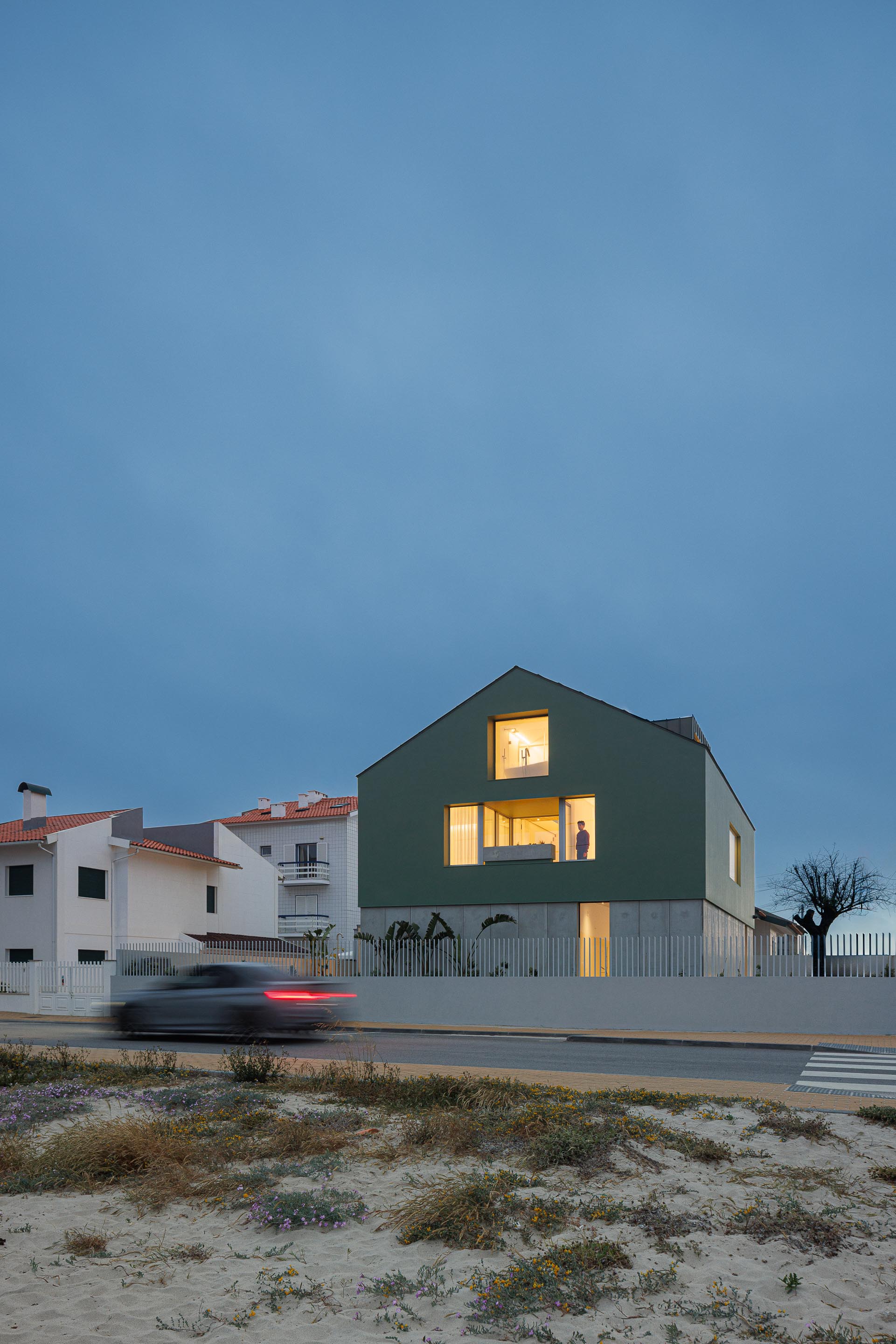Moradia de volume compacto verde com cobertura inclinada e mansarda, iluminada ao entardecer, vista da rua — Casa Verde arquitectura M2 Senos Arquitectos fotografia Ivo Tavares