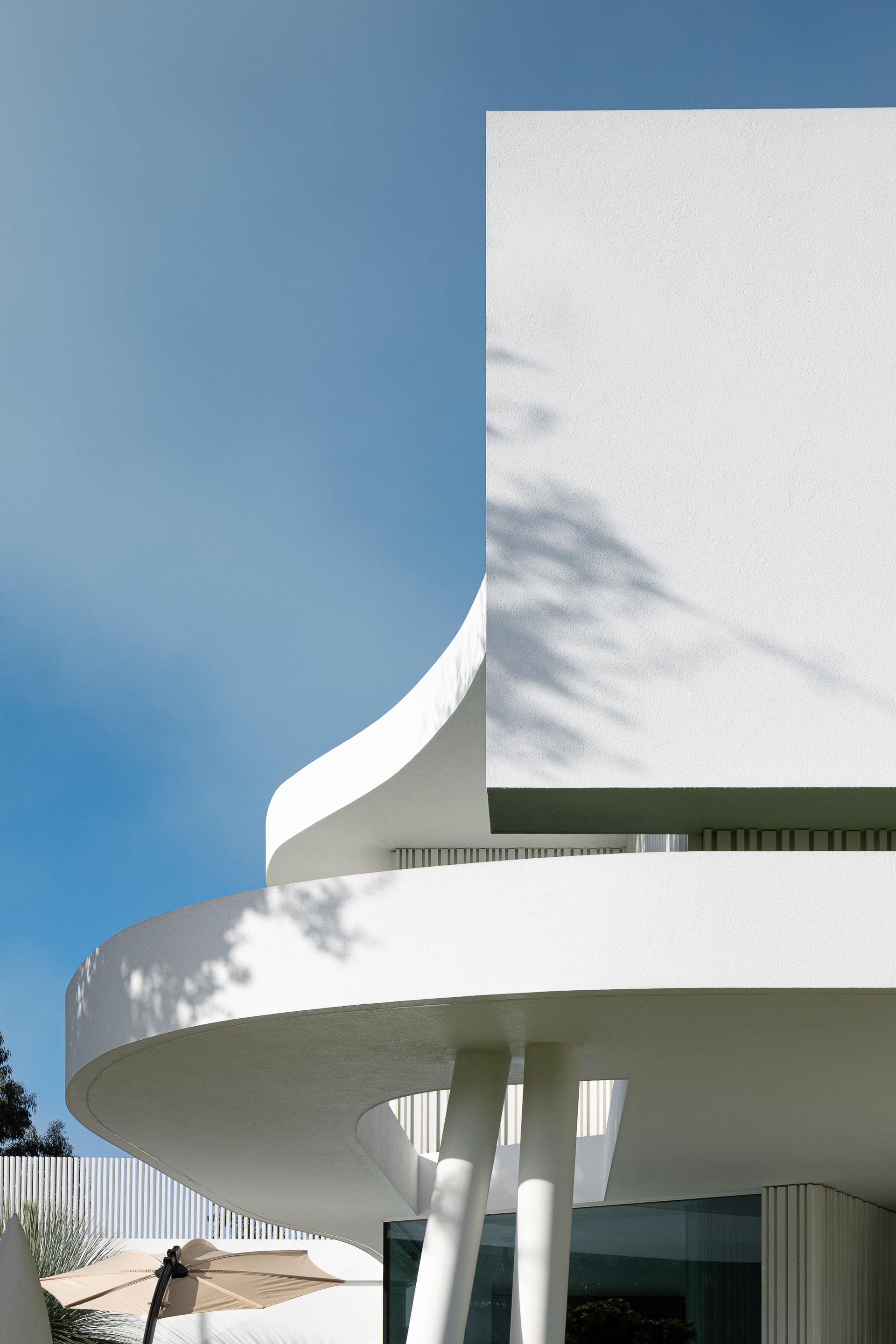 Varanda curva em betão branco com pilares inclinados, criando formas orgânicas e dinâmicas na fachada — RiscoWhite arquitectura Risco Singular – Arquitectura, Lda. fotografia Ivo Tavares