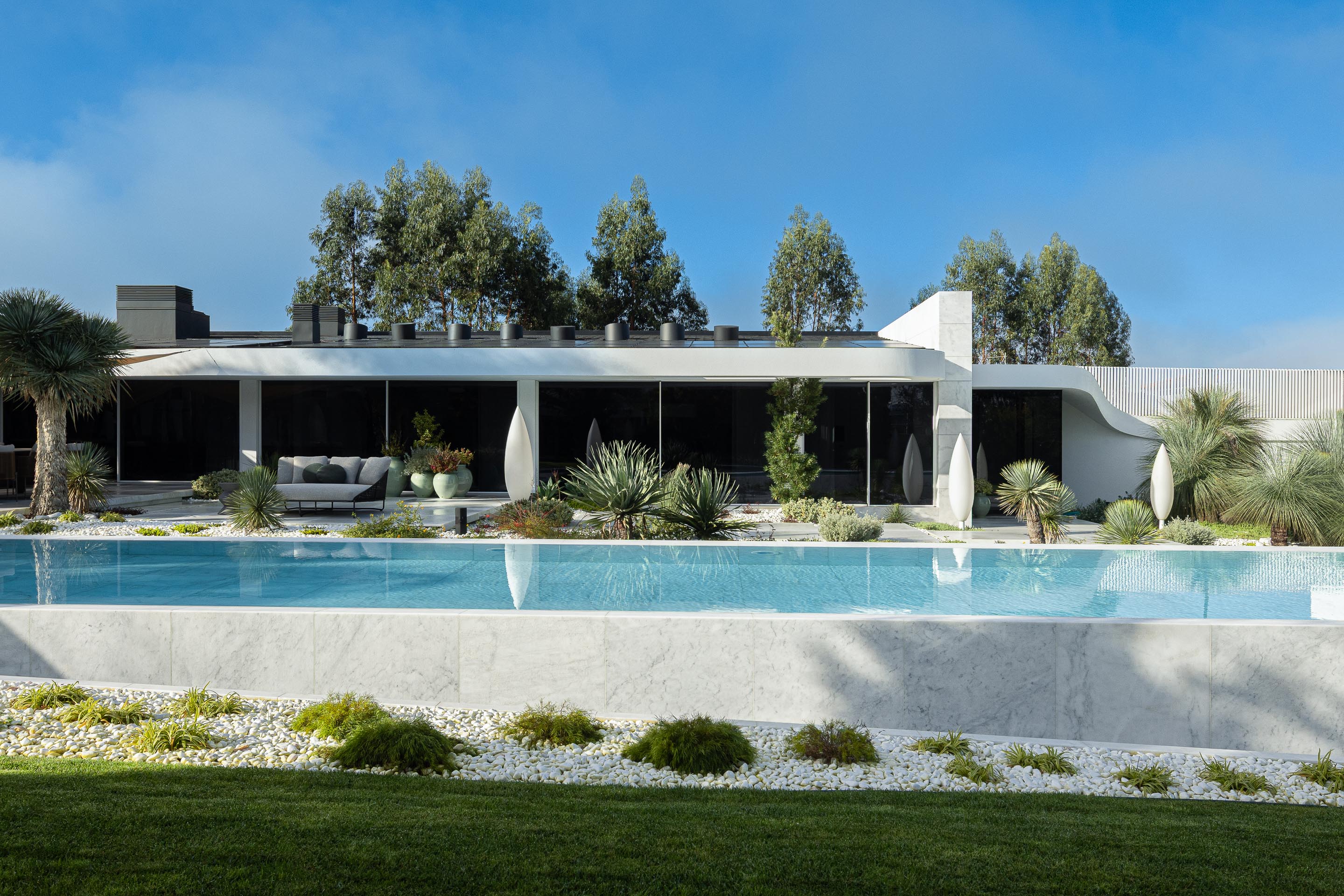 Fachada posterior da moradia com volume horizontal, grandes vãos escurecidos e piscina infinita em mármore branco — RiscoWhite arquitectura Risco Singular – Arquitectura, Lda. fotografia Ivo Tavares