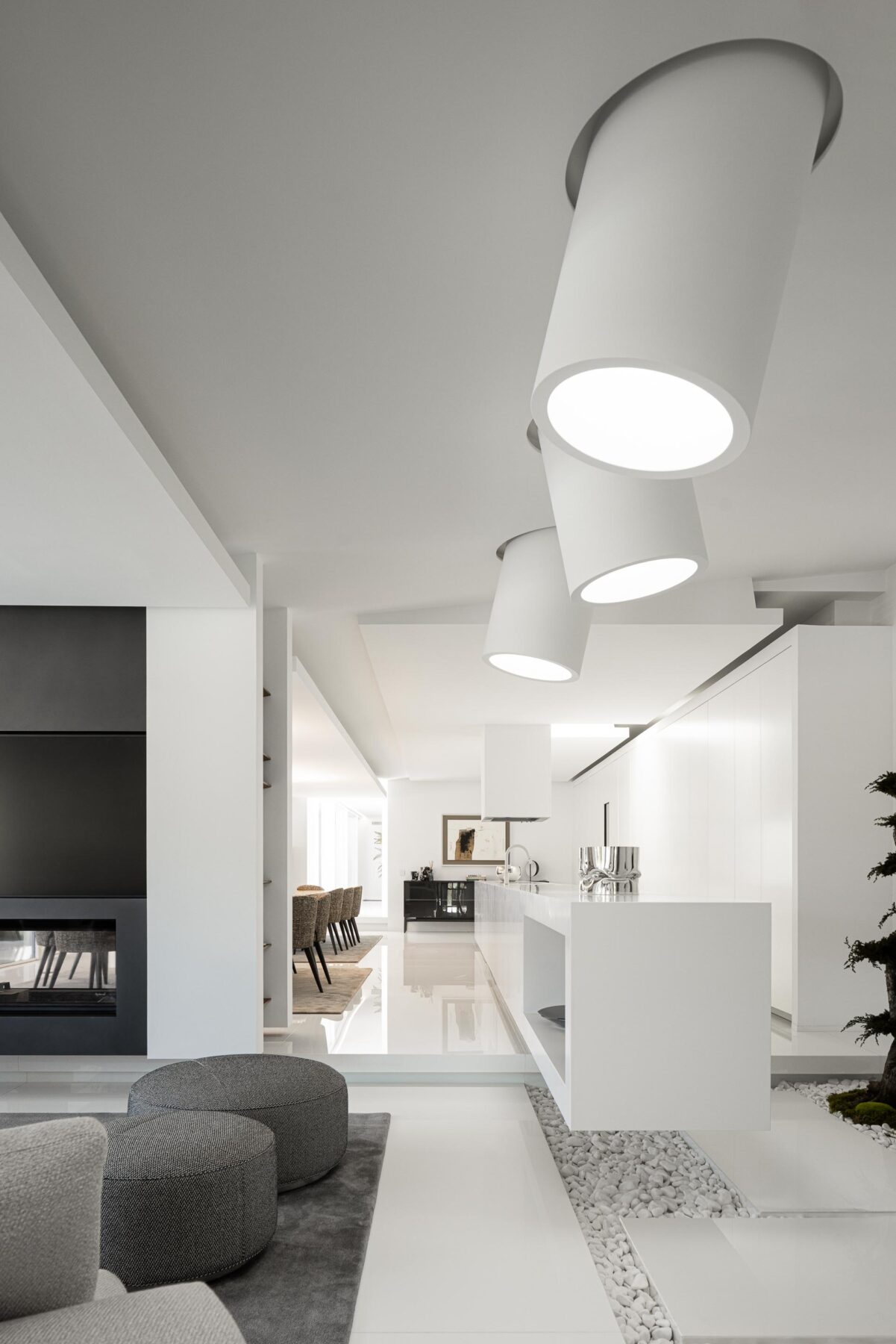 Interior de sala e cozinha em open-space, com pavimento branco polido e candeeiros cilíndricos suspensos — RiscoWhite arquitectura Risco Singular – Arquitectura, Lda. fotografia Ivo Tavares