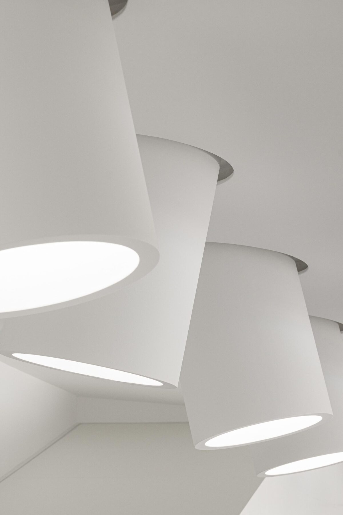 Detalhe de candeeiros cilíndricos brancos suspensos do teto, criando iluminação pontual e design minimalista — RiscoWhite arquitectura Risco Singular – Arquitectura, Lda. fotografia Ivo Tavares