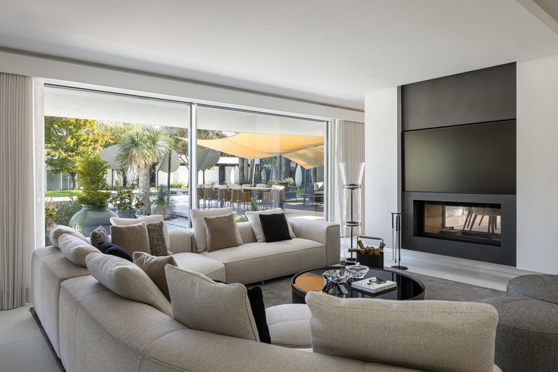 Sala de estar com sofá em L, lareira embutida e grande vão envidraçado com vista para o jardim exterior — RiscoWhite arquitectura Risco Singular – Arquitectura, Lda. fotografia Ivo Tavares