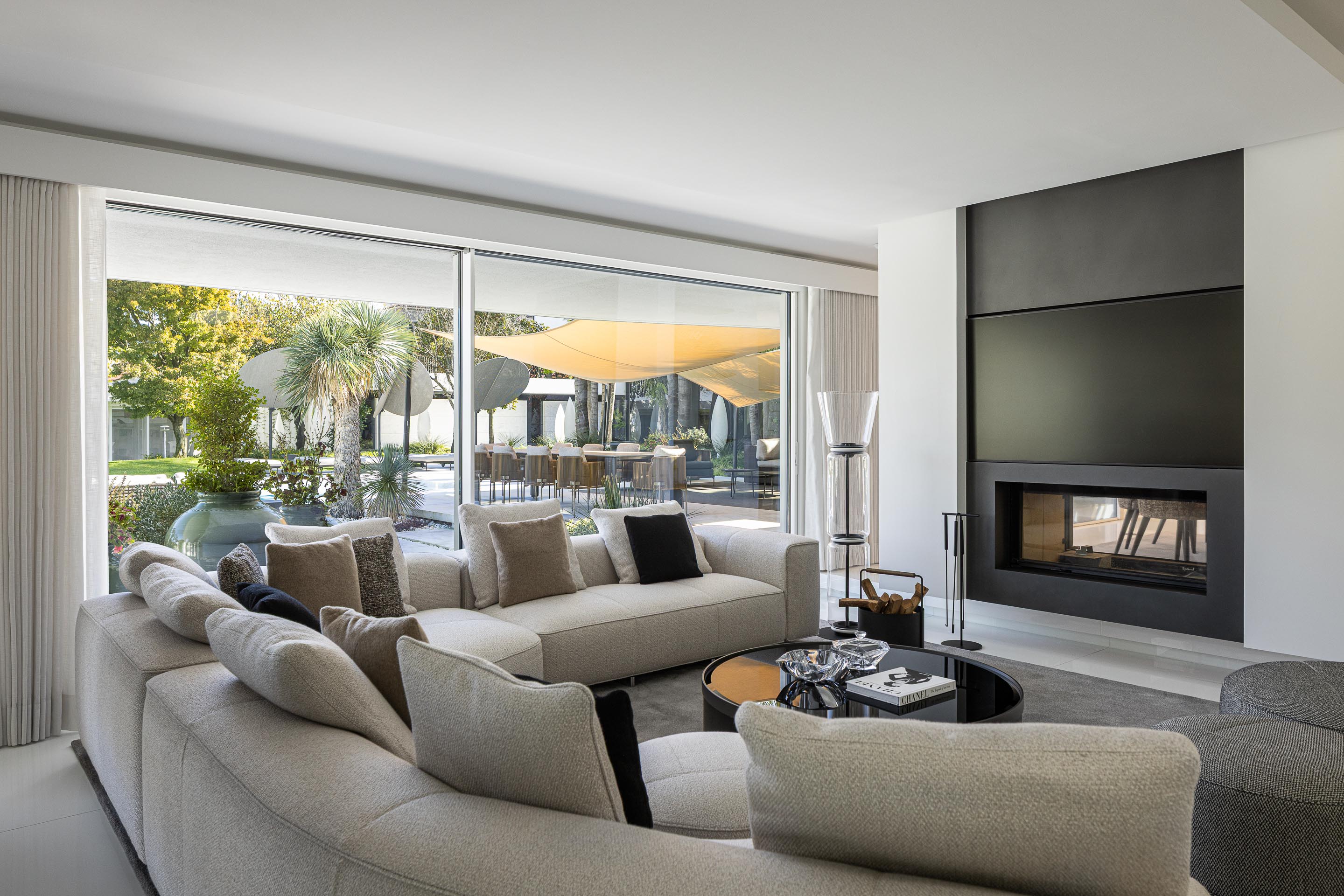 Sala de estar com sofá em L, lareira embutida e grande vão envidraçado com vista para o jardim exterior — RiscoWhite arquitectura Risco Singular – Arquitectura, Lda. fotografia Ivo Tavares