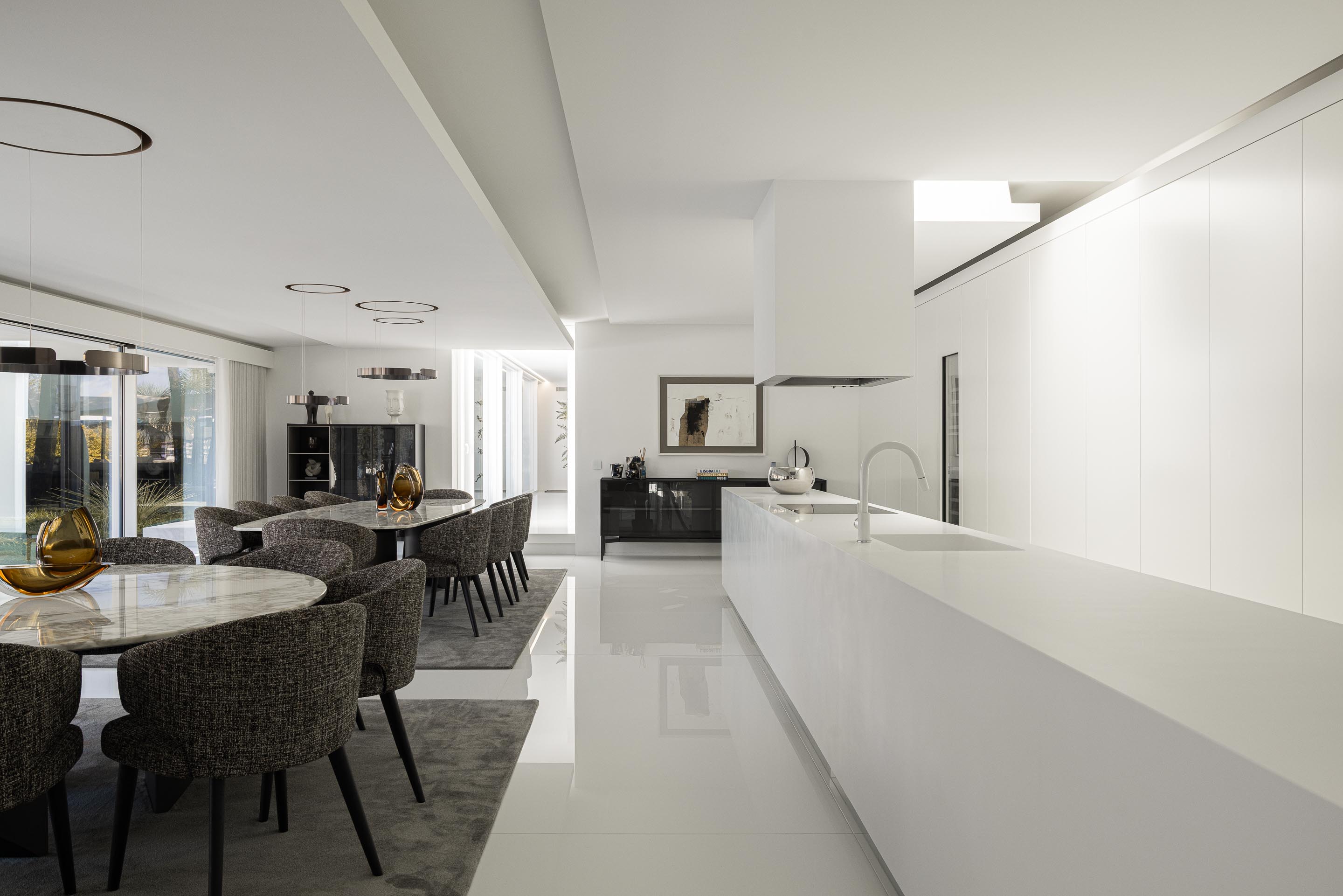 Cozinha com ilha central branca e zona de refeições com mesa em mármore, num espaço amplo e luminoso — RiscoWhite arquitectura Risco Singular – Arquitectura, Lda. fotografia Ivo Tavares