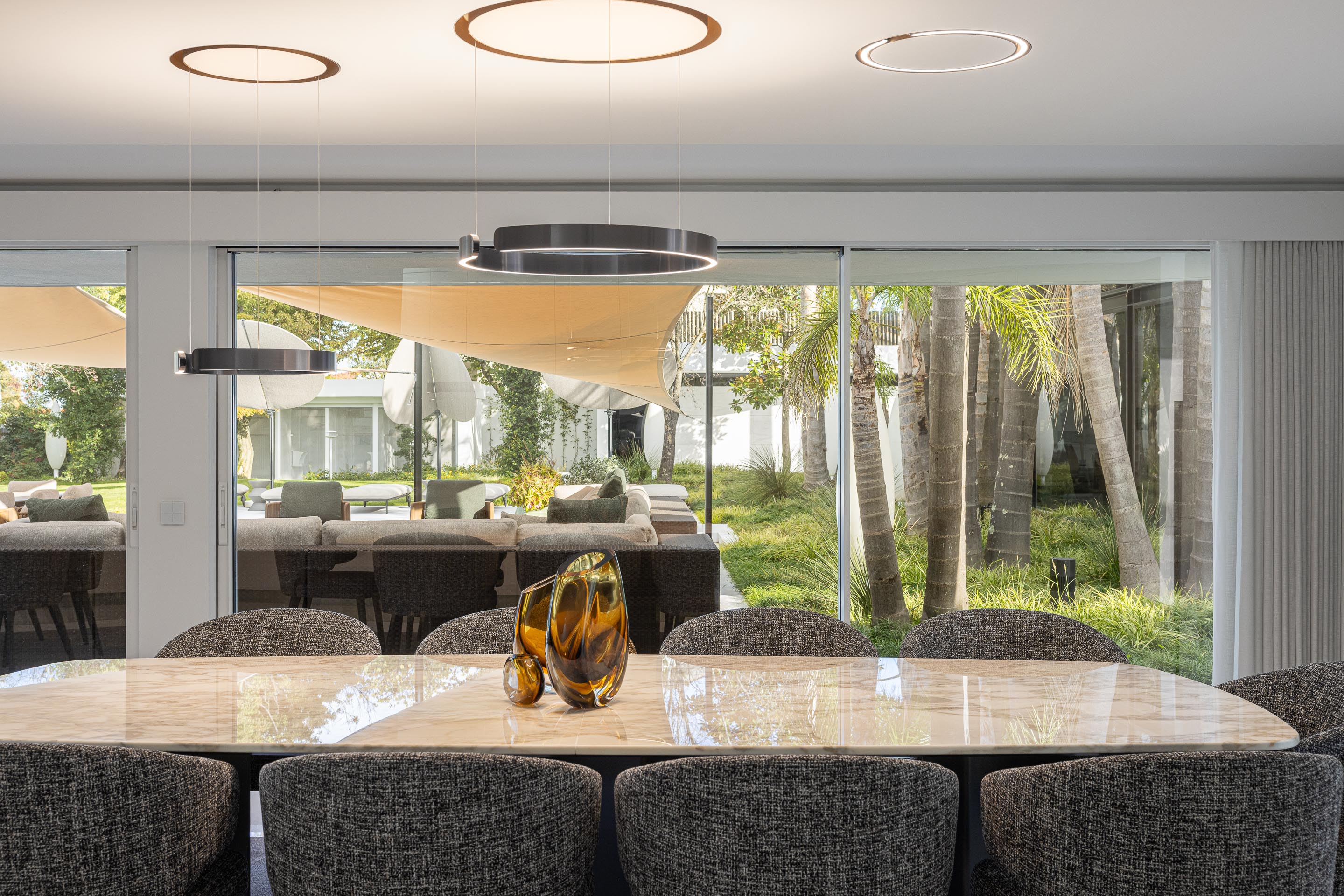 Zona de refeições com mesa em mármore e cadeiras estofadas, com vista para o exterior e candeeiros circulares — RiscoWhite arquitectura Risco Singular – Arquitectura, Lda. fotografia Ivo Tavares
