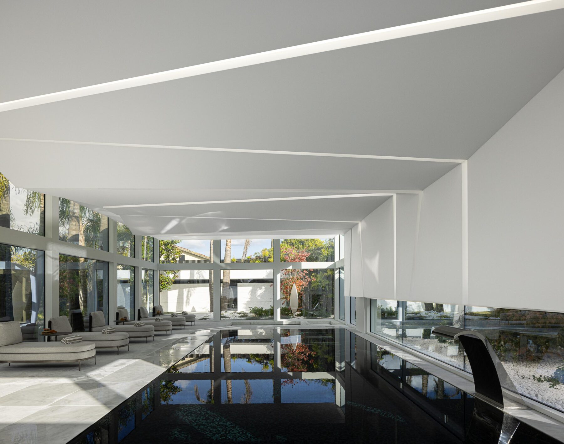 Piscina interior com grandes vãos envidraçados, pavimento em mármore e espreguiçadeiras, criando continuidade exterior — RiscoWhite arquitectura Risco Singular – Arquitectura, Lda. fotografia Ivo Tavares