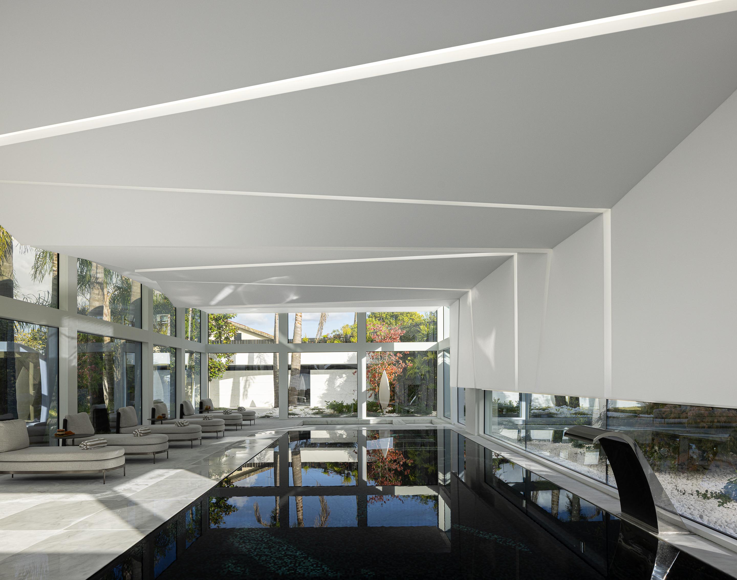 Piscina interior com grandes vãos envidraçados, pavimento em mármore e espreguiçadeiras, criando continuidade exterior — RiscoWhite arquitectura Risco Singular – Arquitectura, Lda. fotografia Ivo Tavares