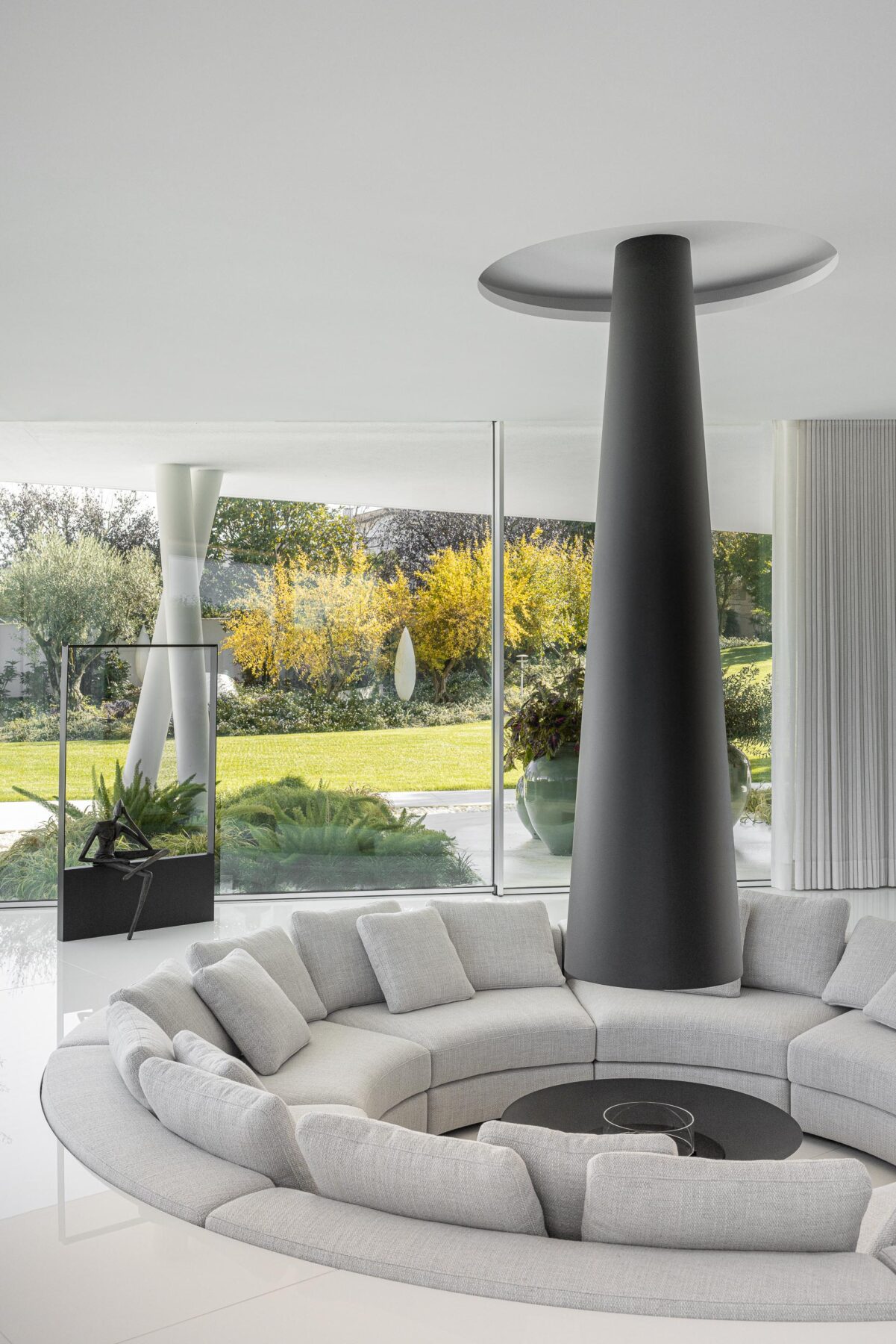 Sala de estar circular com sofá curvo e lareira cónica central, rodeada por grandes vãos envidraçados — RiscoWhite arquitectura Risco Singular – Arquitectura, Lda. fotografia Ivo Tavares