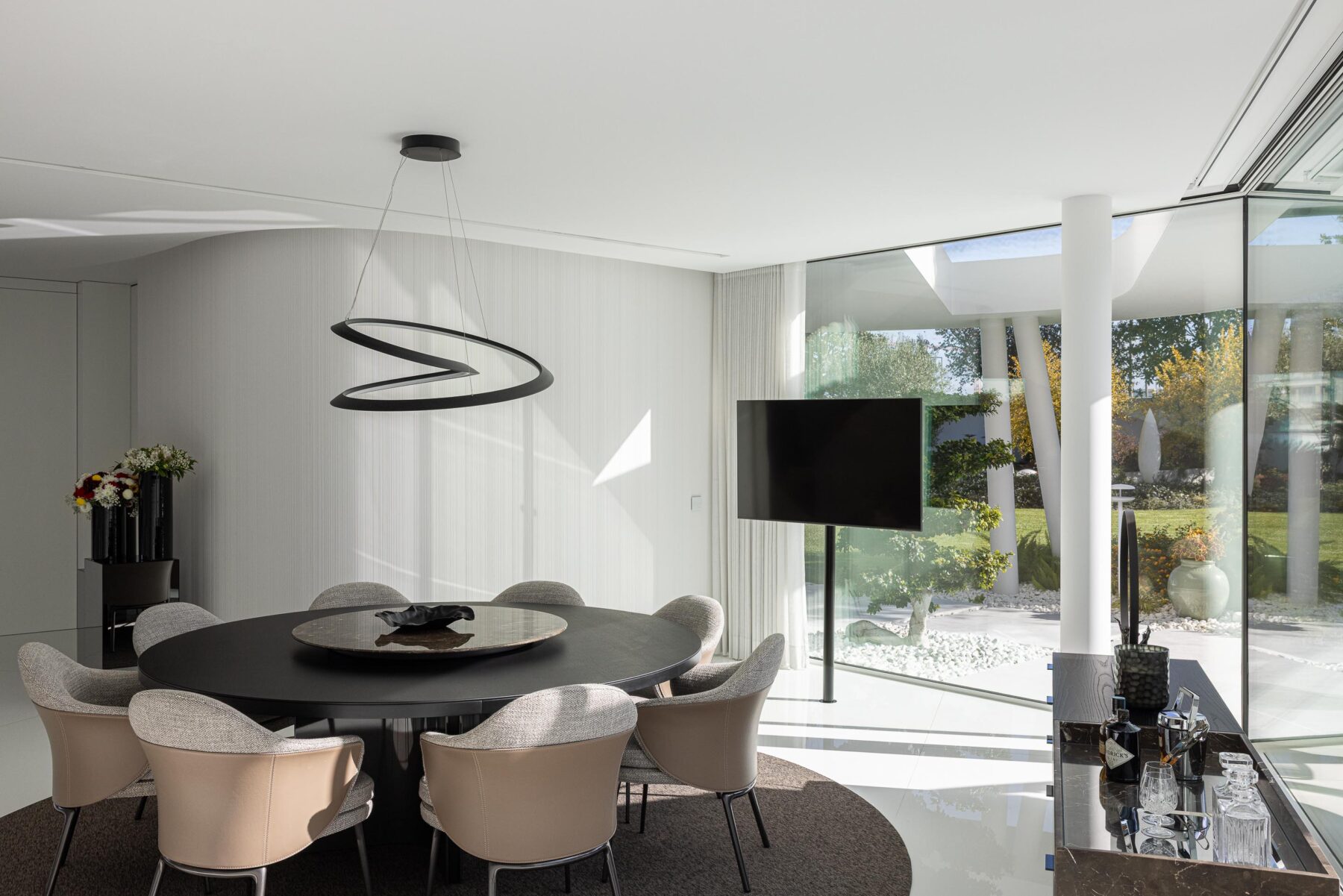 Zona de refeições com mesa redonda escura e candeeiro suspenso de design, com vista para o jardim — RiscoWhite arquitectura Risco Singular – Arquitectura, Lda. fotografia Ivo Tavares