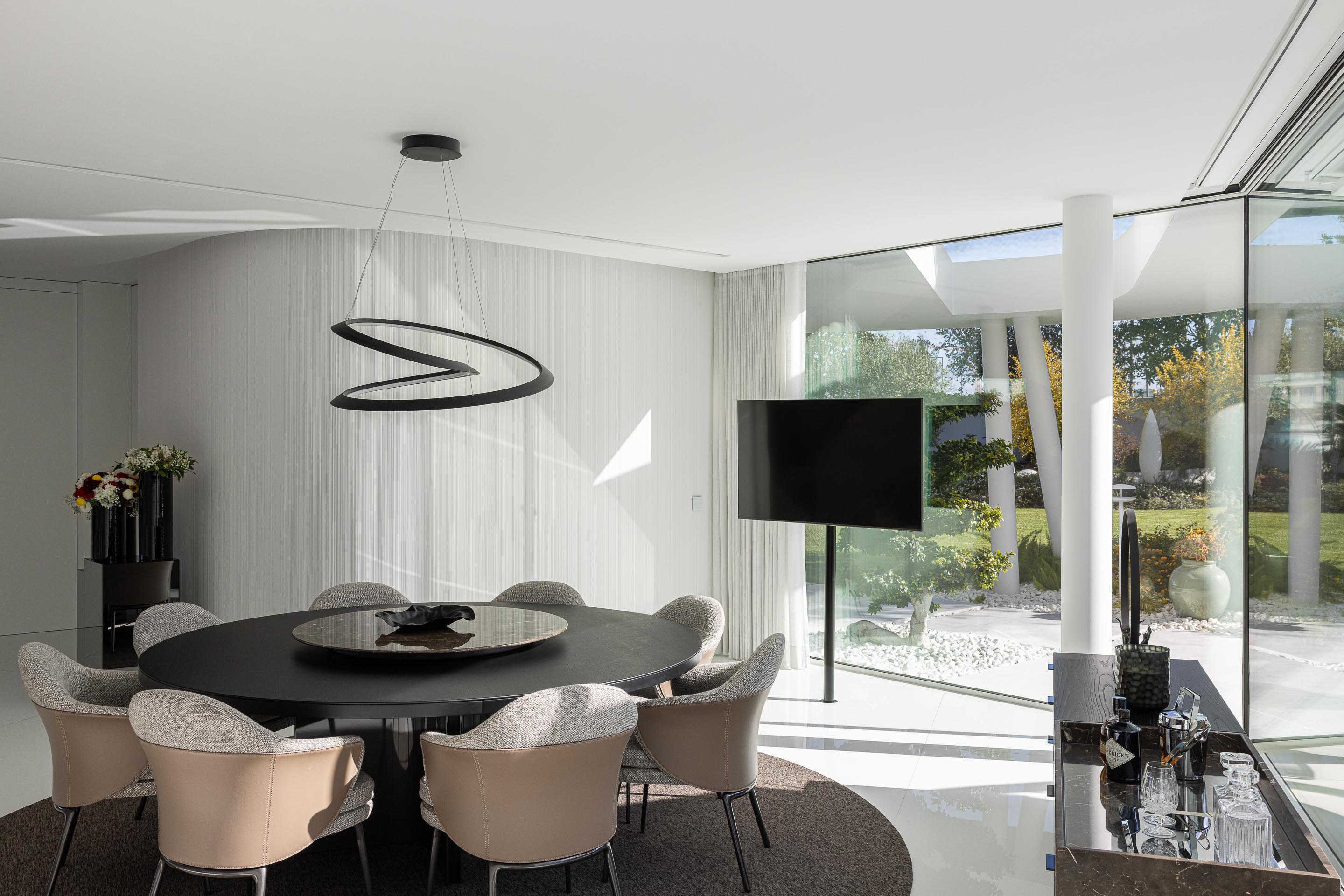 Zona de refeições com mesa redonda escura e candeeiro suspenso de design, com vista para o jardim — RiscoWhite arquitectura Risco Singular – Arquitectura, Lda. fotografia Ivo Tavares
