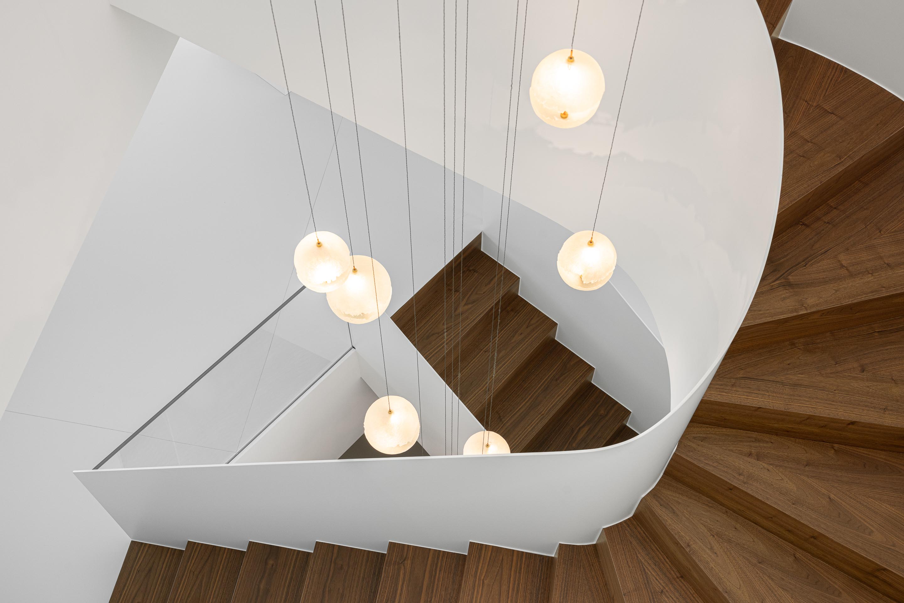Escada em caracol com degraus em madeira de nogueira e guarda-corpos branco, iluminada por candeeiros esféricos — RiscoWhite arquitectura Risco Singular – Arquitectura, Lda. fotografia Ivo Tavares