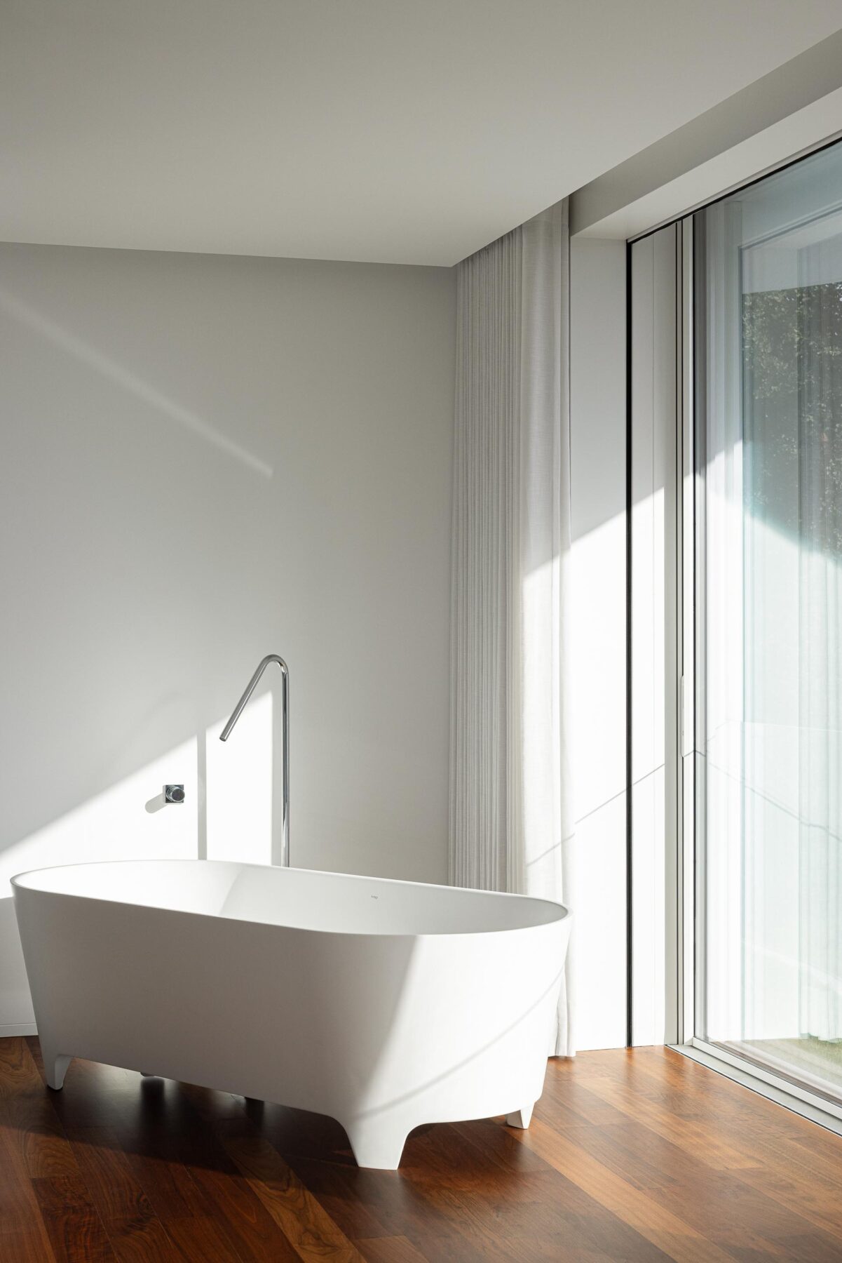 Casa de banho com banheira freestanding branca, pavimento em madeira e grande vão envidraçado — RiscoWhite arquitectura Risco Singular – Arquitectura, Lda. fotografia Ivo Tavares
