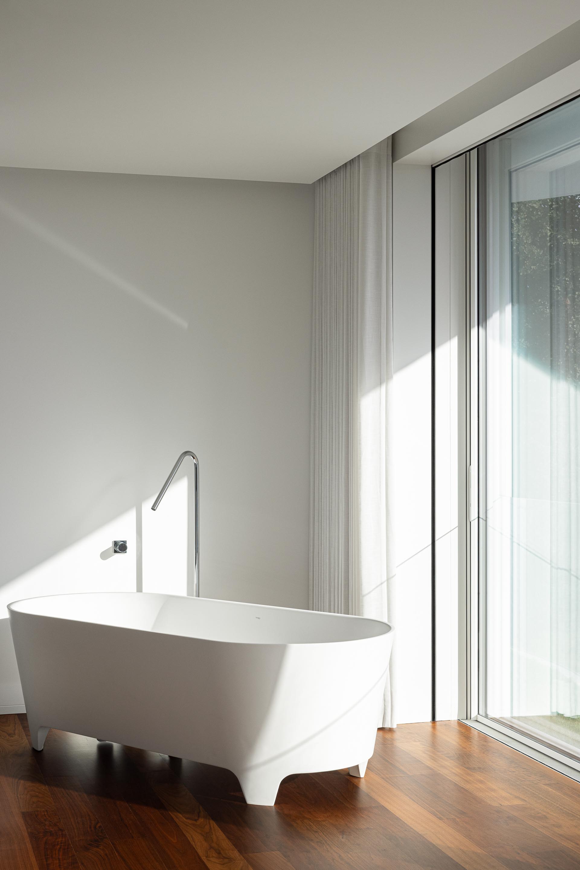Casa de banho com banheira freestanding branca, pavimento em madeira e grande vão envidraçado — RiscoWhite arquitectura Risco Singular – Arquitectura, Lda. fotografia Ivo Tavares