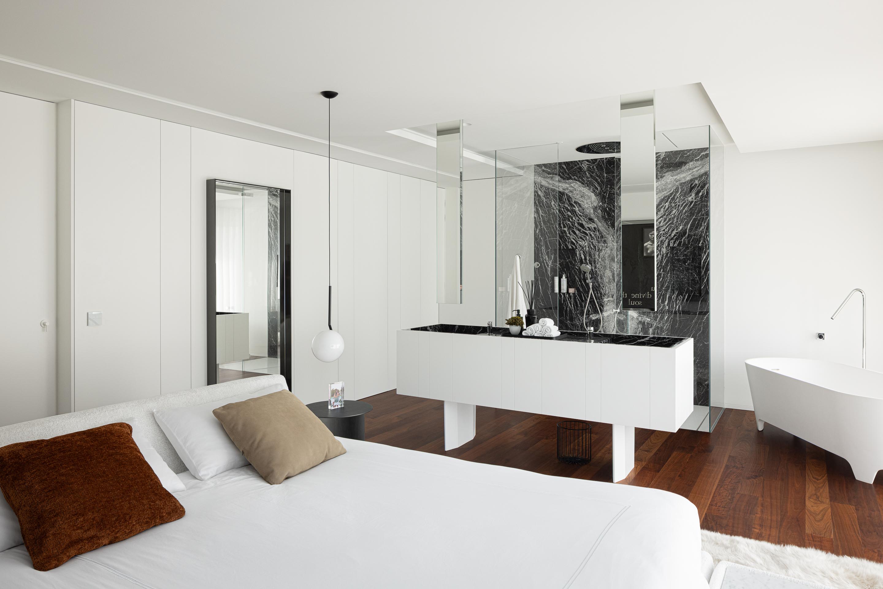 Quarto com pavimento em madeira, banheira freestanding e casa de banho integrada com lavatório e mármore negro — RiscoWhite arquitectura Risco Singular – Arquitectura, Lda. fotografia Ivo Tavares