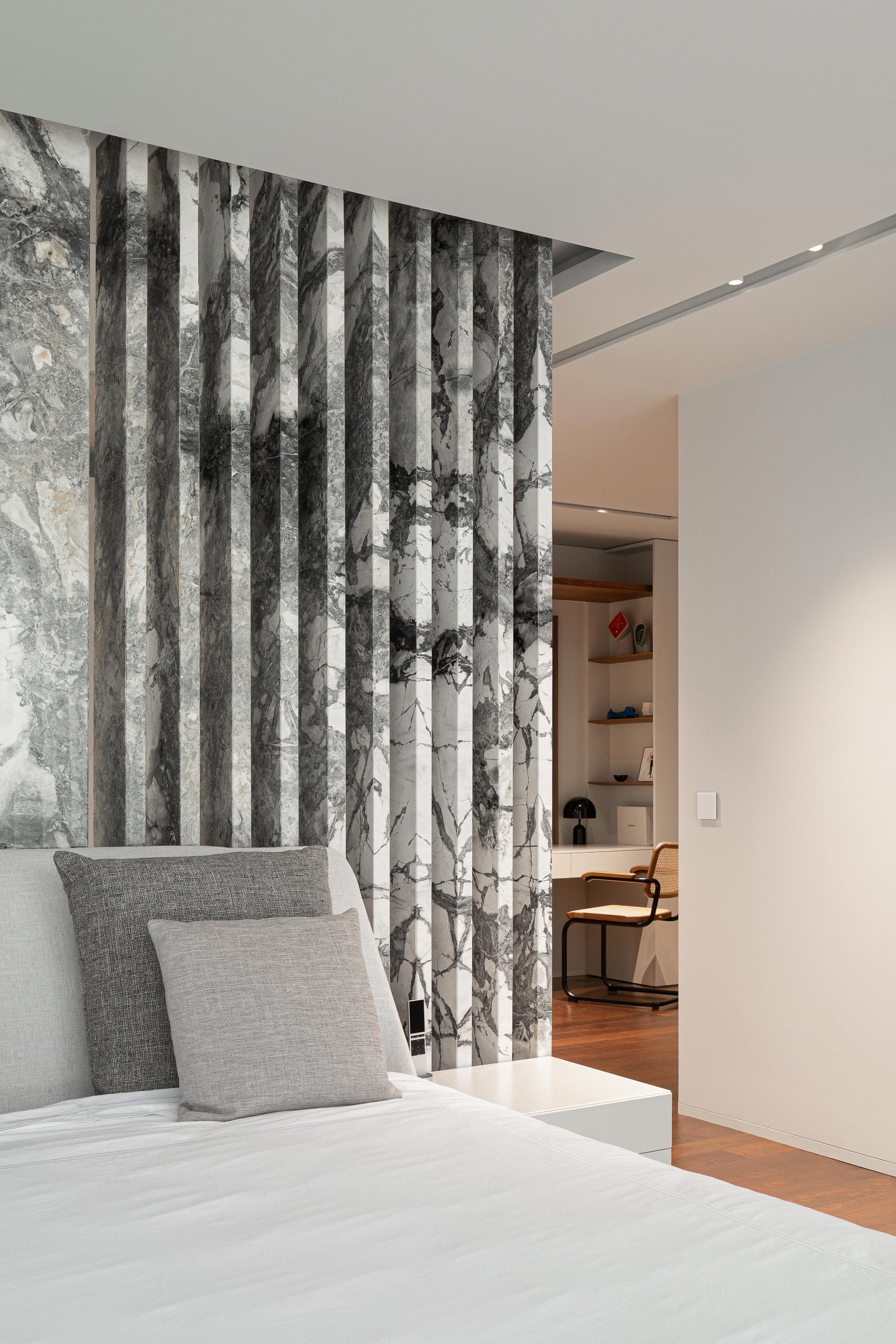 Detalhe da cabeceira do quarto com painel de mármore cinzento e ripado vertical, criando textura e profundidade — RiscoWhite arquitectura Risco Singular – Arquitectura, Lda. fotografia Ivo Tavares