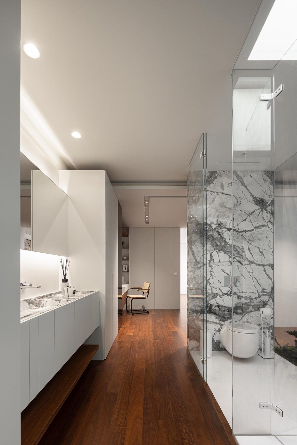 Corredor com pavimento em madeira, lavatório suspenso e casa de banho com divisória de vidro e iluminação zenital — RiscoWhite arquitectura Risco Singular – Arquitectura, Lda. fotografia Ivo Tavares