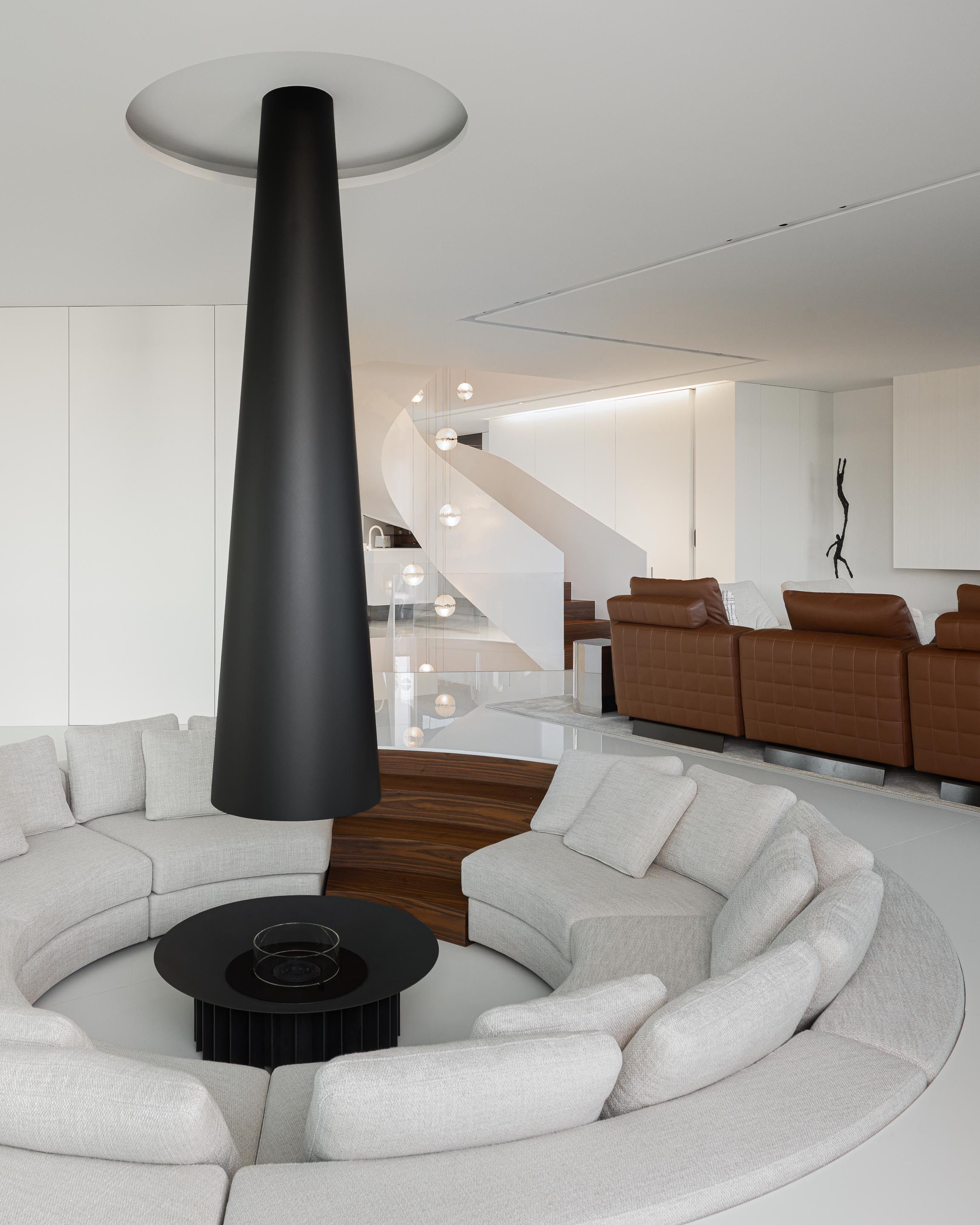 Sala de estar circular com lareira cónica preta e sofá curvo, com vista para a escada em caracol — RiscoWhite arquitectura Risco Singular – Arquitectura, Lda. fotografia Ivo Tavares