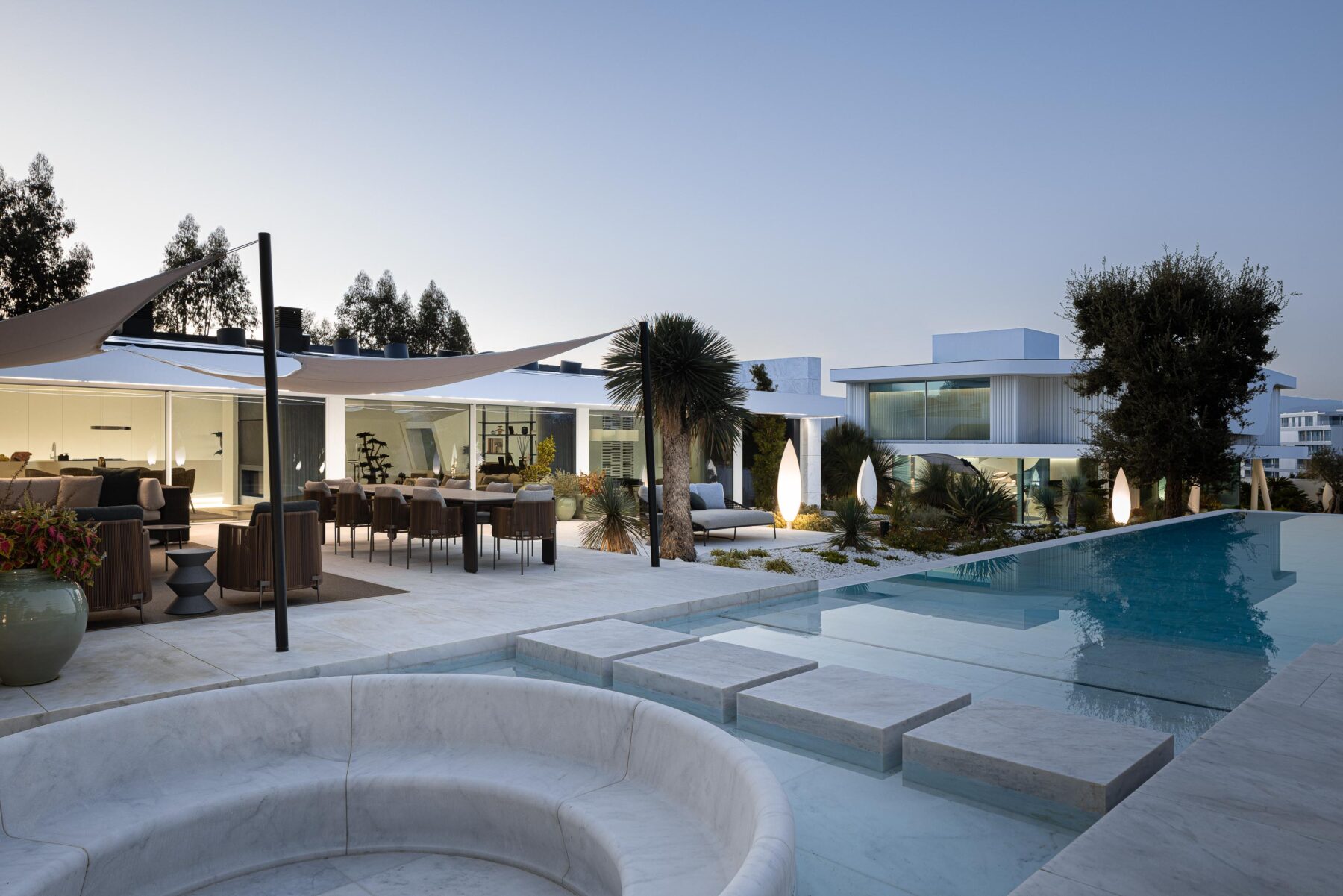 Vista exterior ao anoitecer da moradia e piscina, com iluminação integrada destacando os volumes e a água — RiscoWhite arquitectura Risco Singular – Arquitectura, Lda. fotografia Ivo Tavares