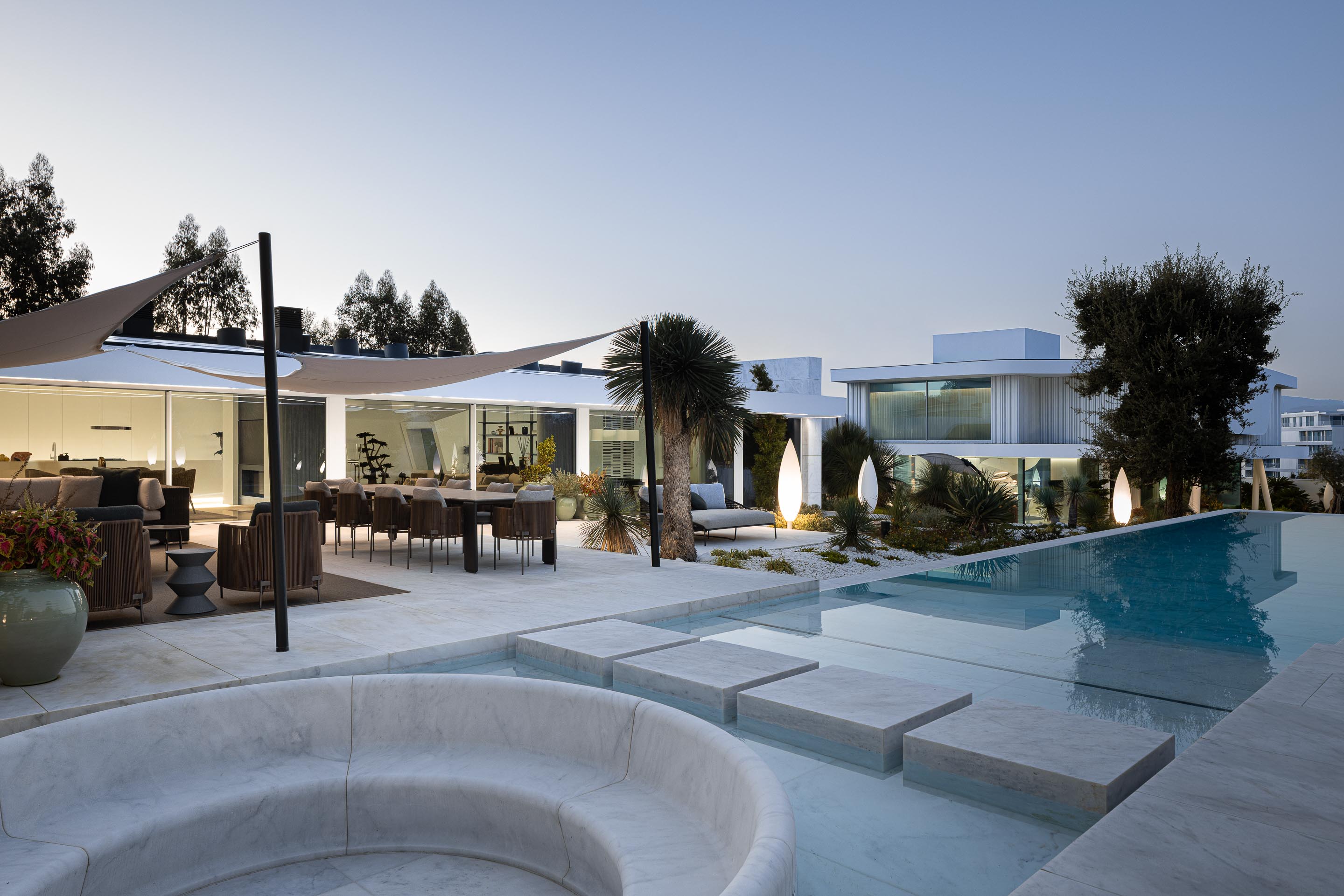 Vista exterior ao anoitecer da moradia e piscina, com iluminação integrada destacando os volumes e a água — RiscoWhite arquitectura Risco Singular – Arquitectura, Lda. fotografia Ivo Tavares