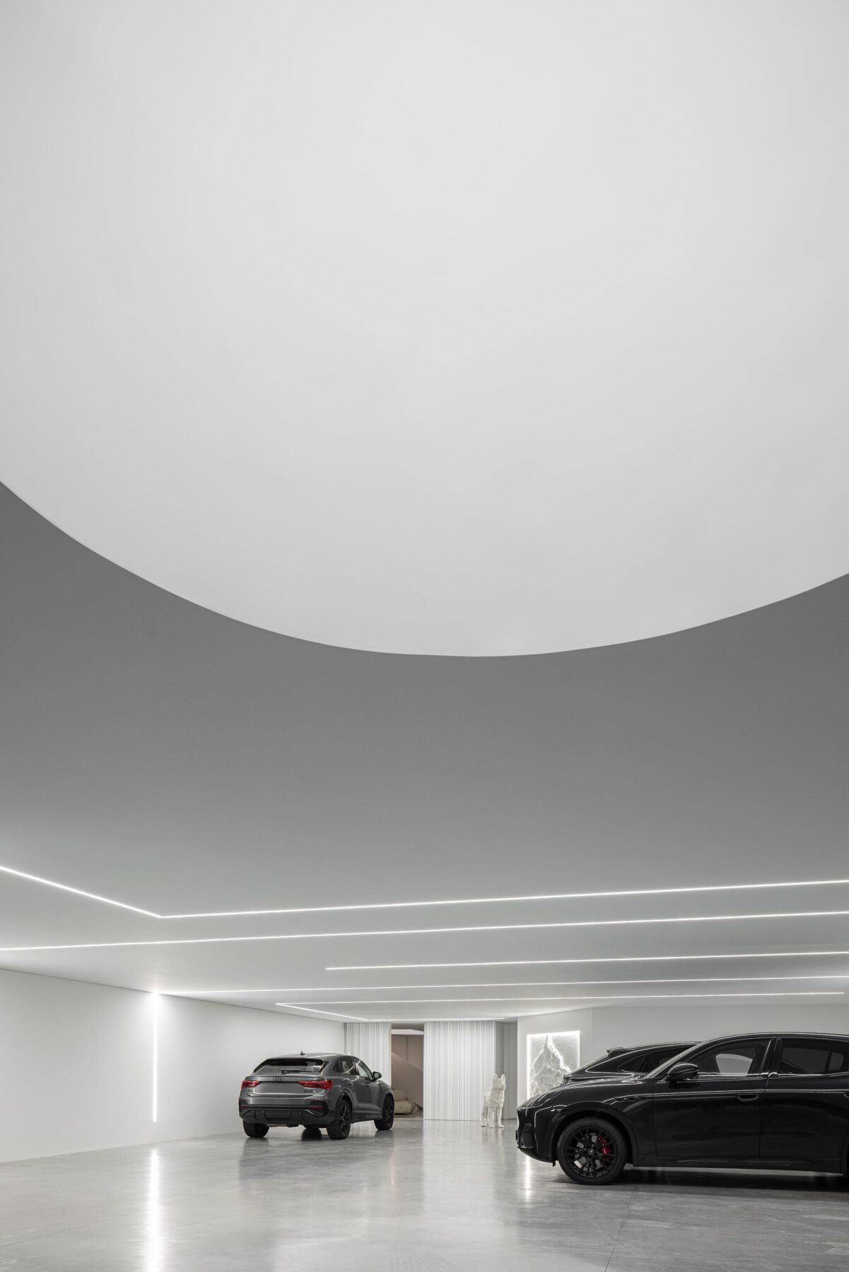 Garagem com pavimento em betão cinzento, teto curvo e iluminação linear embutida, criando um espaço amplo — RiscoWhite arquitectura Risco Singular – Arquitectura, Lda. fotografia Ivo Tavares