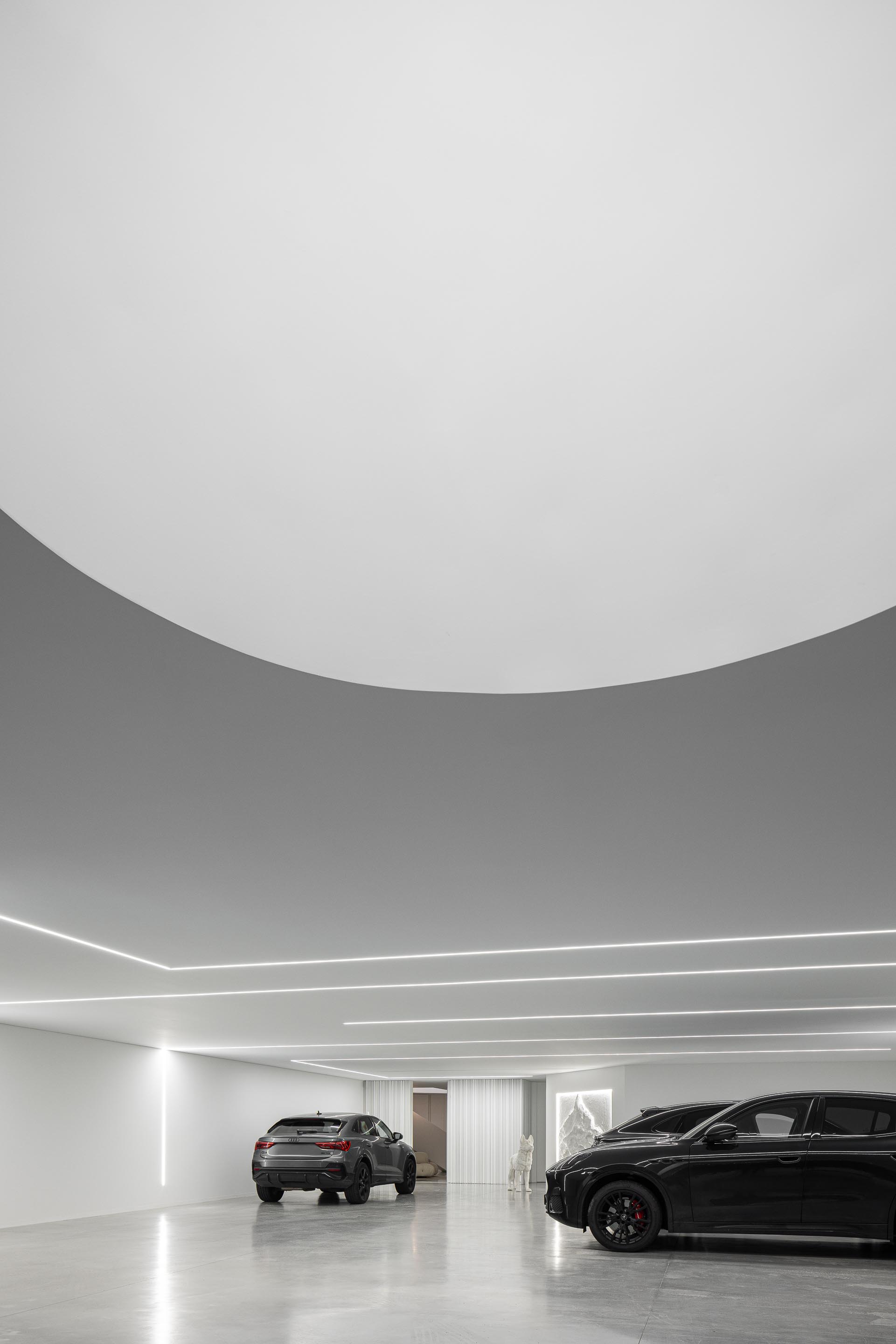 Garagem com pavimento em betão cinzento, teto curvo e iluminação linear embutida, criando um espaço amplo — RiscoWhite arquitectura Risco Singular – Arquitectura, Lda. fotografia Ivo Tavares