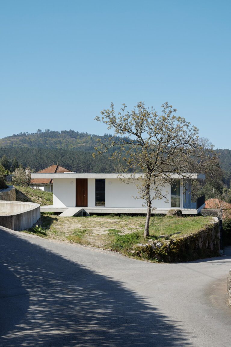 Moradia branca com cobertura plana, implantada em socalco, com entrada em madeira escura e vãos envidraçados — CASA COQUEIRA arquitectura Tiago Sousa Arquitecto fotografia Ivo Tavares