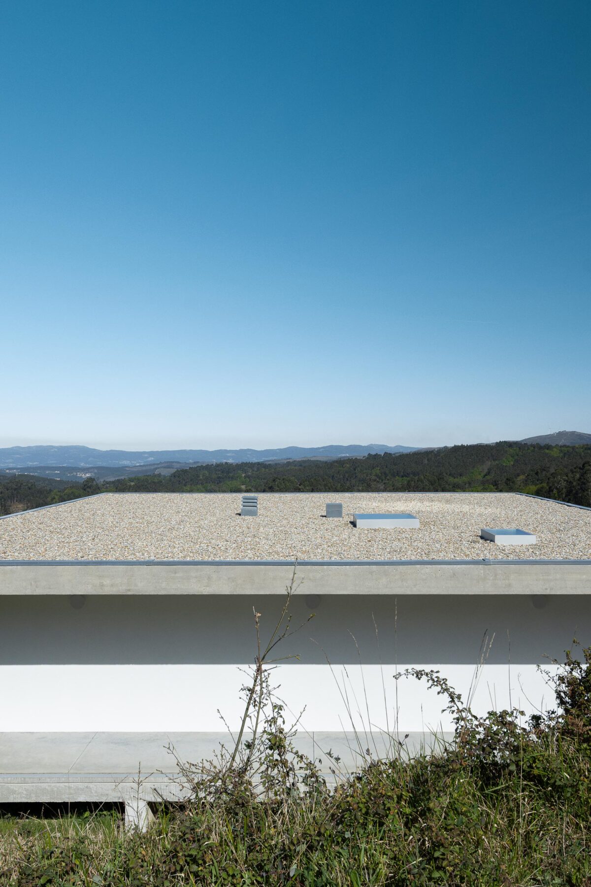 Cobertura plana da moradia em betão aparente, revestida a gravilha, com claraboias e vista para a paisagem — CASA COQUEIRA arquitectura Tiago Sousa Arquitecto fotografia Ivo Tavares