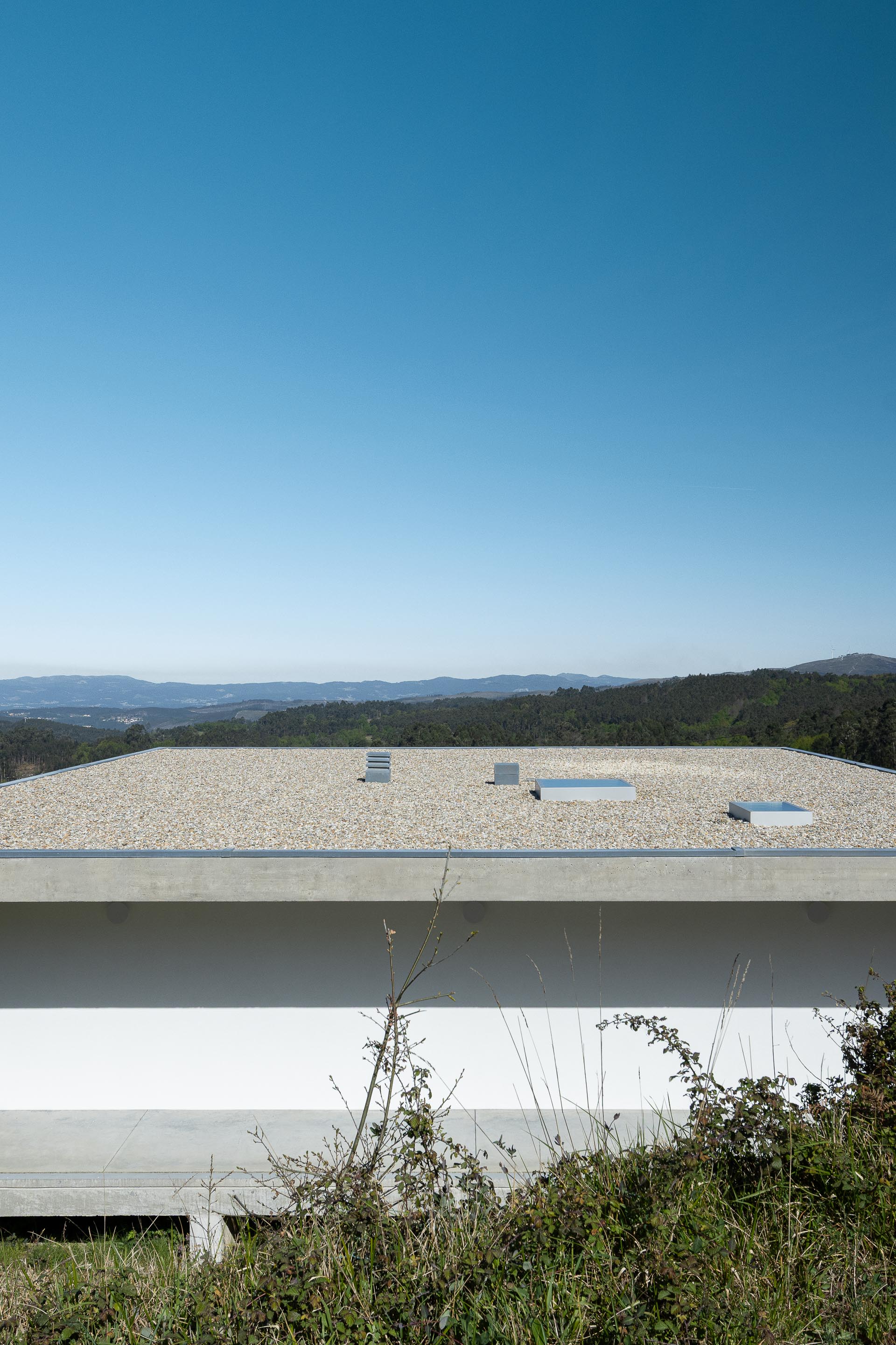 Cobertura plana da moradia em betão aparente, revestida a gravilha, com claraboias e vista para a paisagem — CASA COQUEIRA arquitectura Tiago Sousa Arquitecto fotografia Ivo Tavares