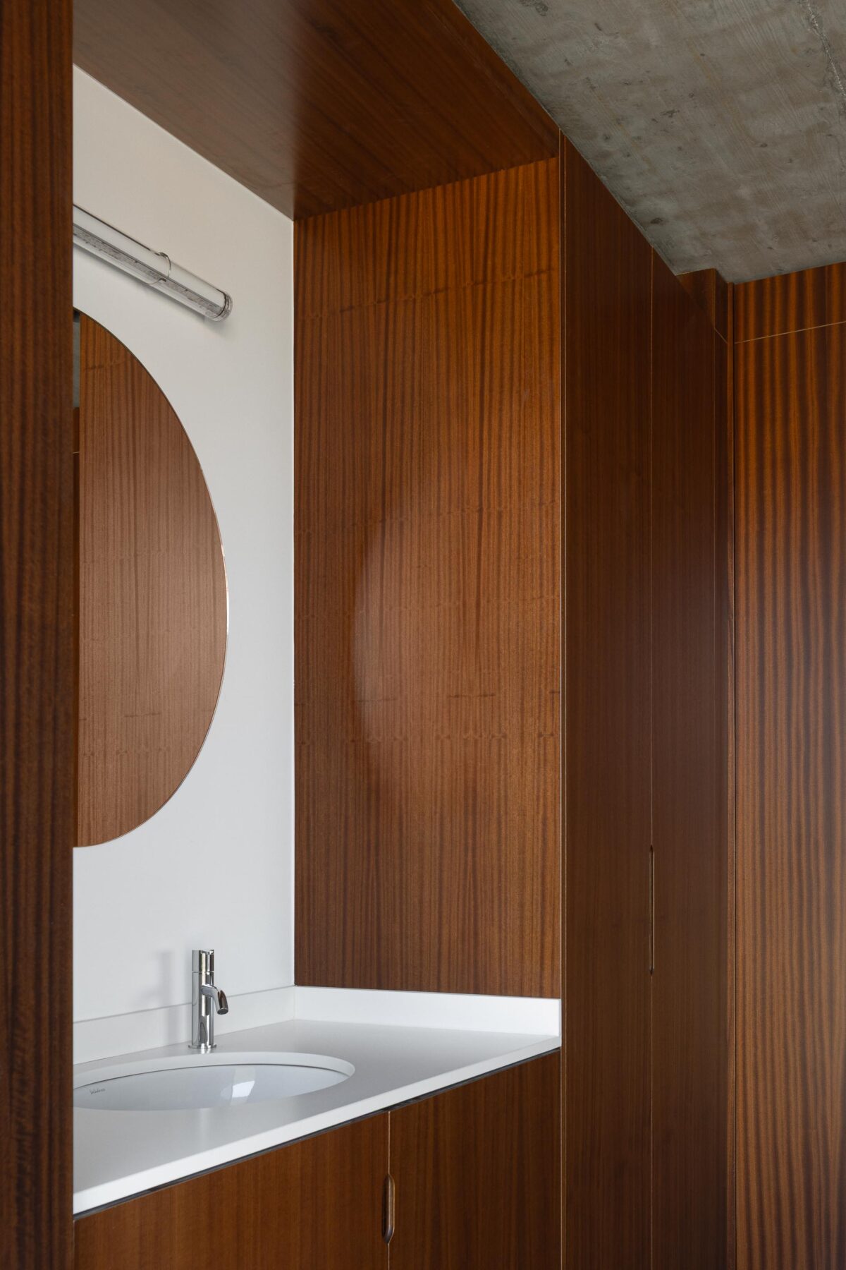 Detalhe do lavatório da casa de banho com bancada branca, armário em madeira escura e espelho redondo. Teto em betão aparente — CASA COQUEIRA arquitectura Tiago Sousa Arquitecto fotografia Ivo Tavares