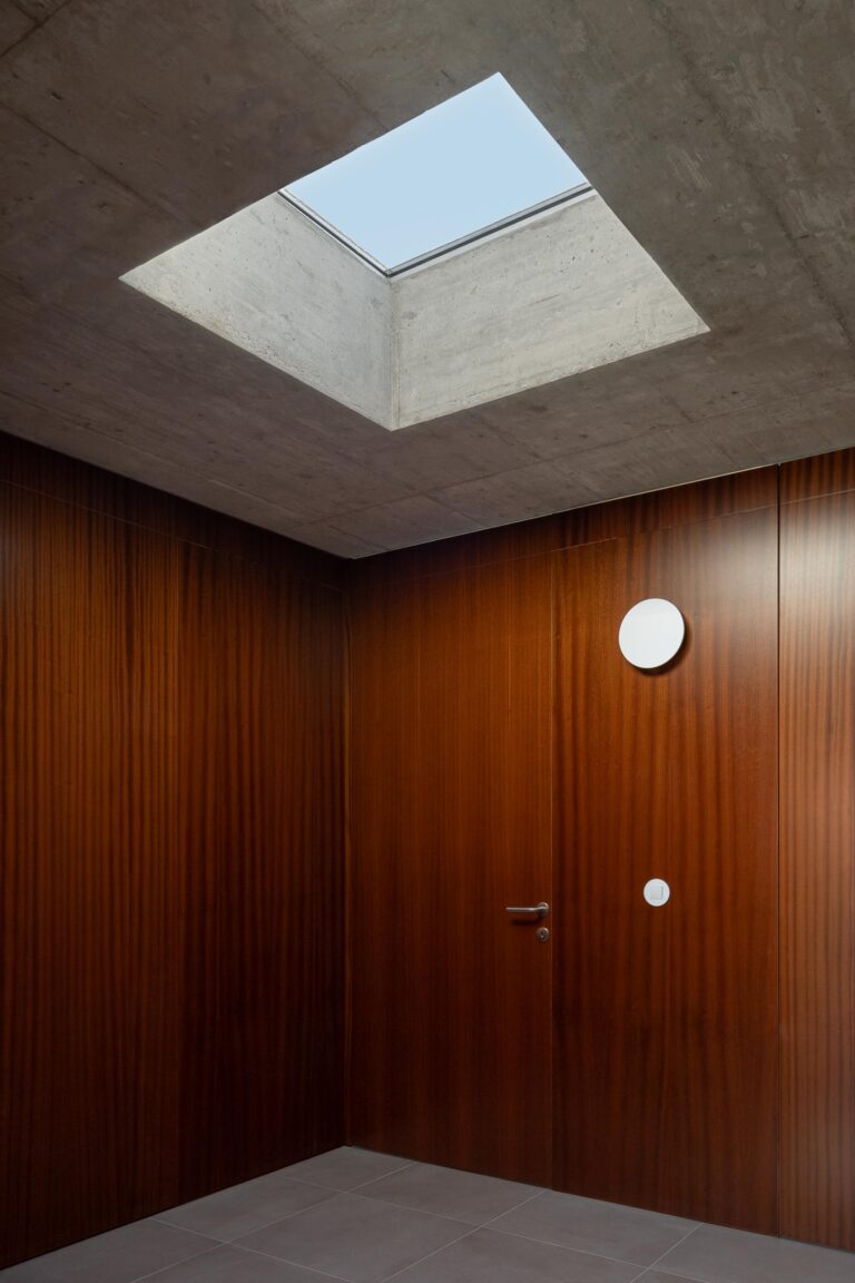 Corredor com paredes e portas em madeira escura, iluminação zenital através de claraboia quadrada no teto de betão — CASA COQUEIRA arquitectura Tiago Sousa Arquitecto fotografia Ivo Tavares