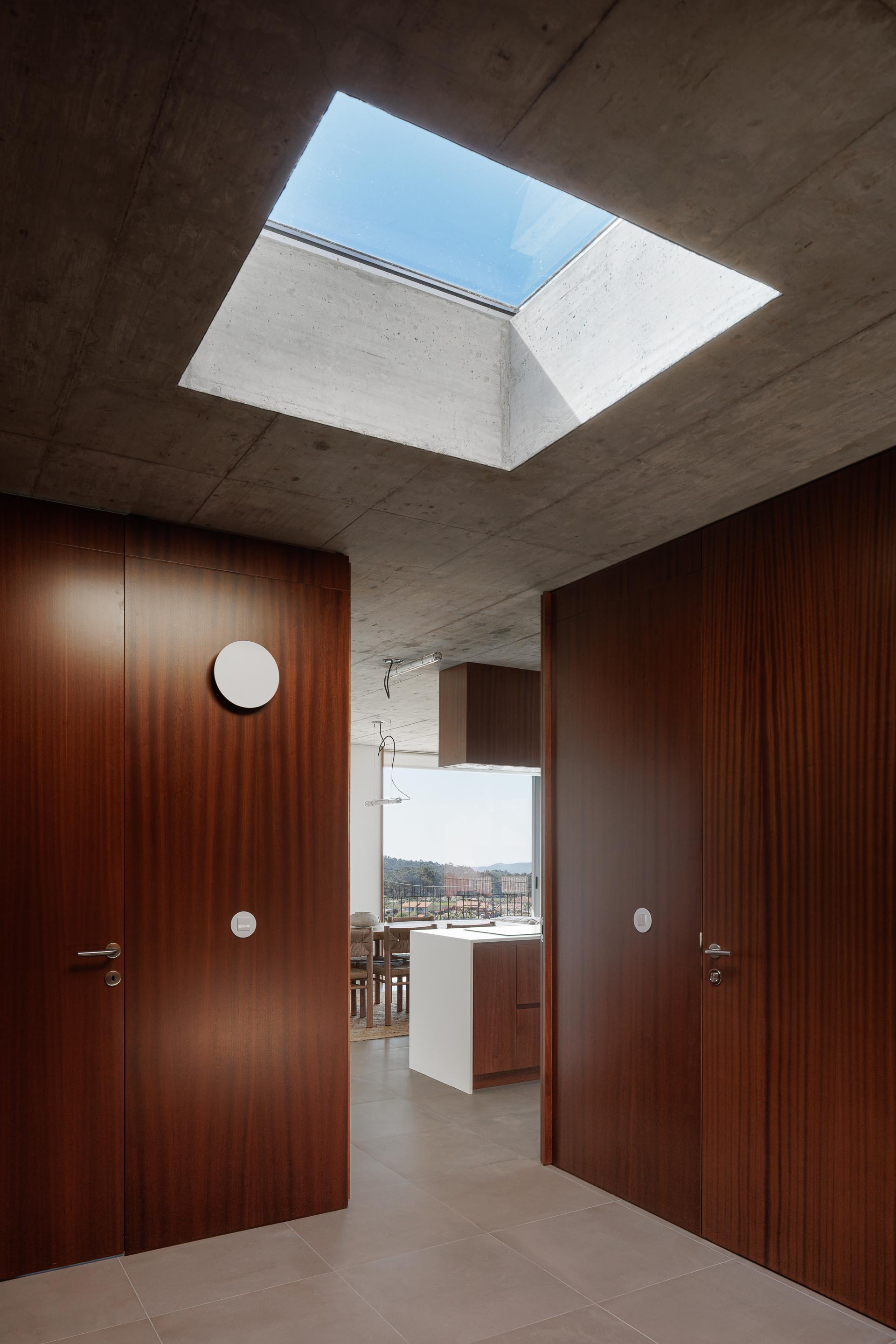 Corredor com portas em madeira escura e iluminação zenital, abrindo para a cozinha e sala de jantar. Teto em betão aparente — CASA COQUEIRA arquitectura Tiago Sousa Arquitecto fotografia Ivo Tavares