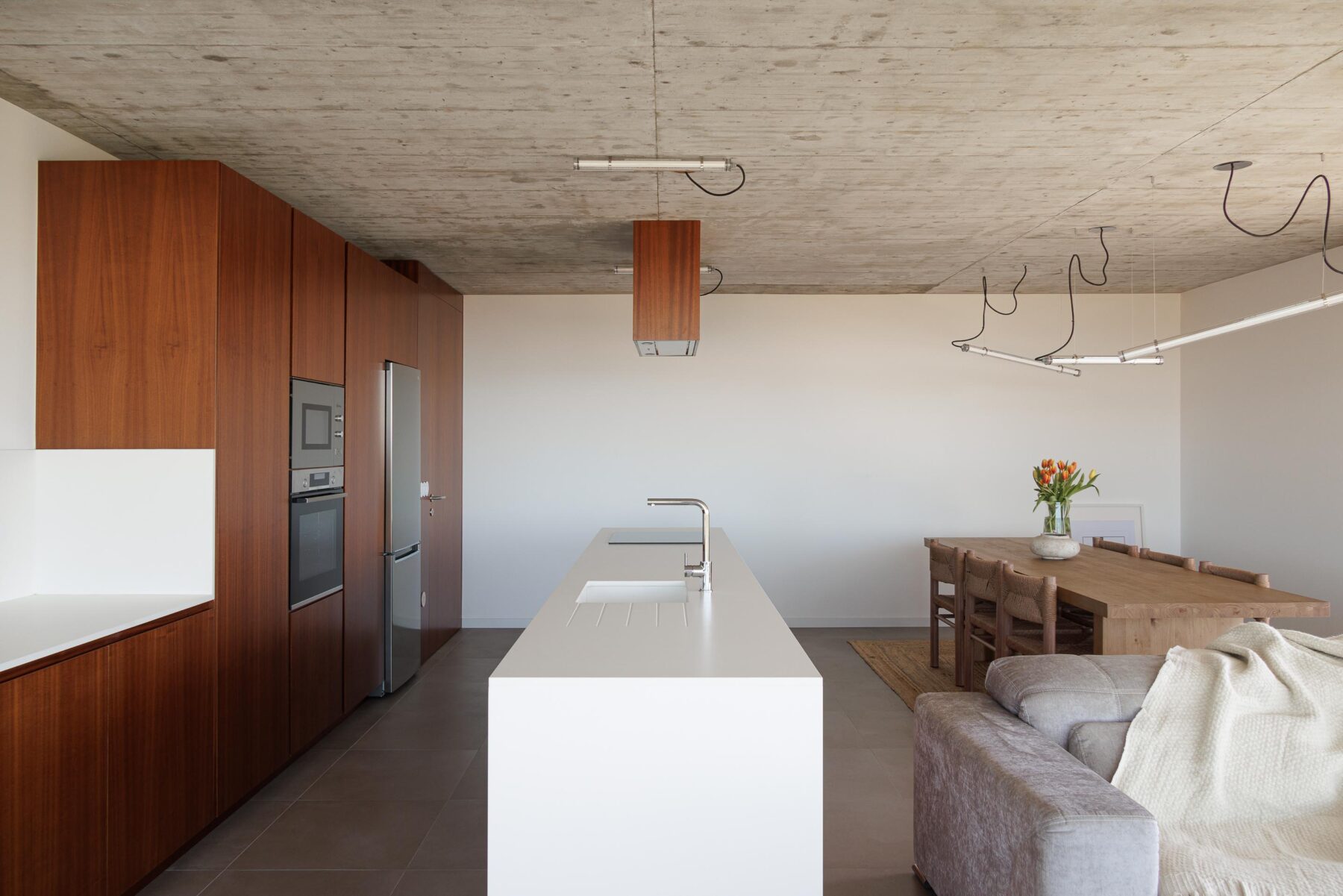 Cozinha e sala de jantar em planta aberta com teto em betão aparente, armários em madeira escura e ilha branca — CASA COQUEIRA arquitectura Tiago Sousa Arquitecto fotografia Ivo Tavares