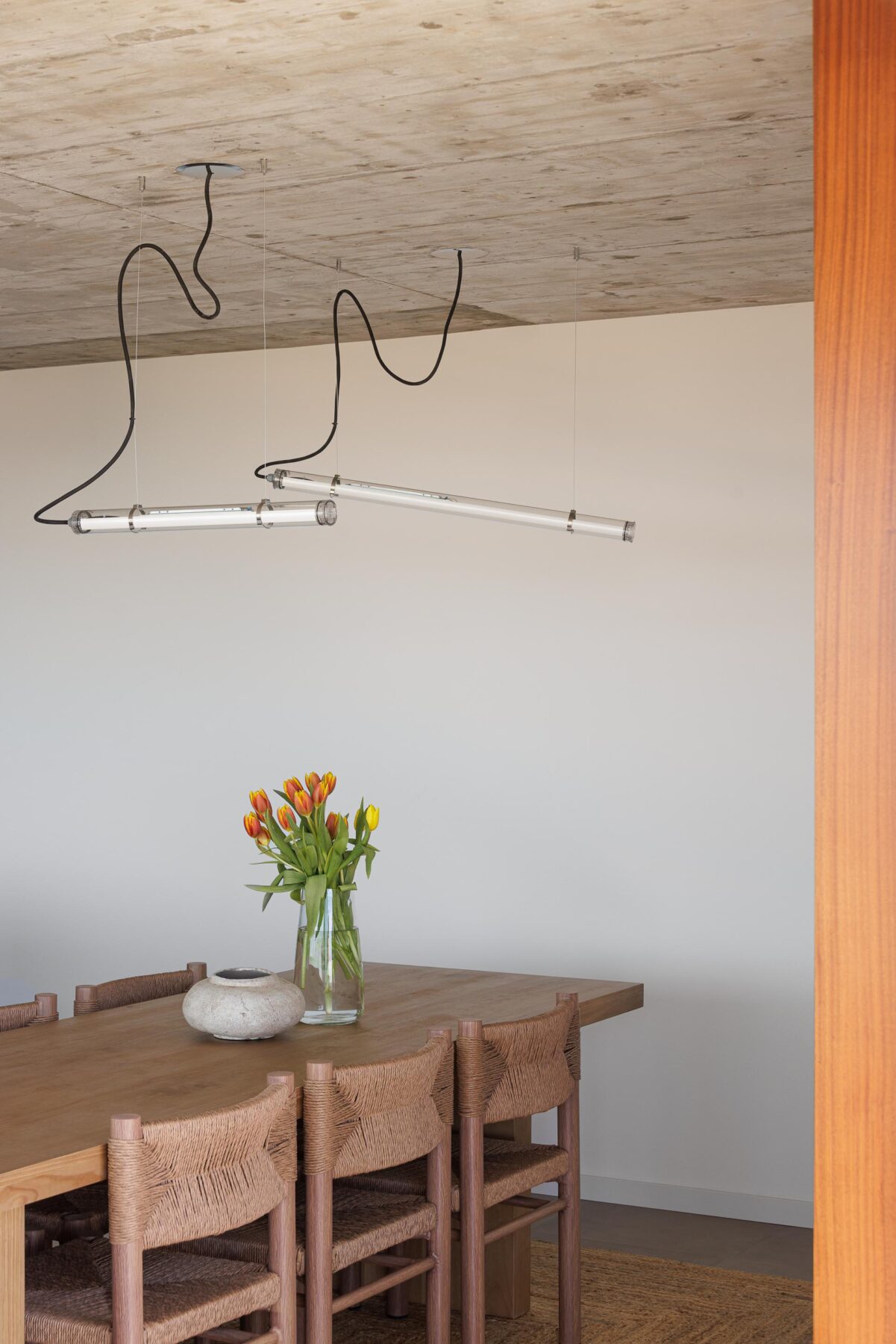 Detalhe da sala de jantar com mesa e cadeiras em madeira, candeeiros tubulares suspensos e teto em betão aparente — CASA COQUEIRA arquitectura Tiago Sousa Arquitecto fotografia Ivo Tavares