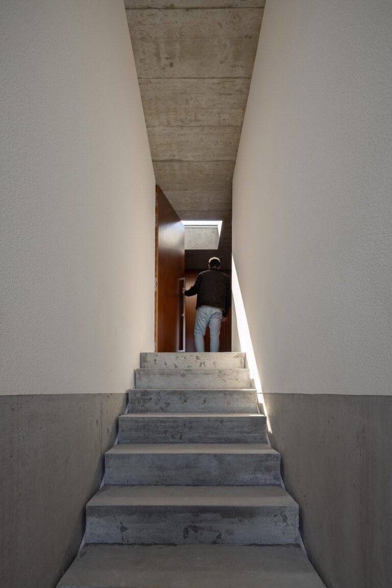 Escadaria de acesso à moradia em betão aparente, ladeada por paredes brancas e teto em betão, com luz zenital — CASA COQUEIRA arquitectura Tiago Sousa Arquitecto fotografia Ivo Tavares