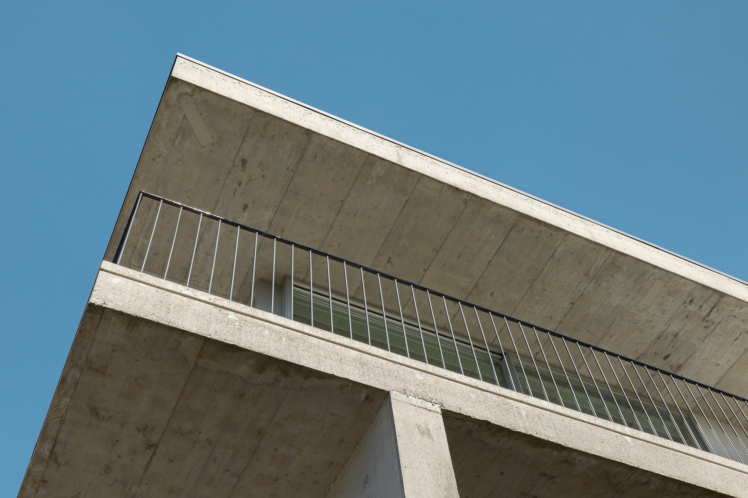 Canto da moradia com estrutura em betão aparente, varanda com guarda-corpos metálicos e grandes vãos envidraçados — CASA COQUEIRA arquitectura Tiago Sousa Arquitecto fotografia Ivo Tavares