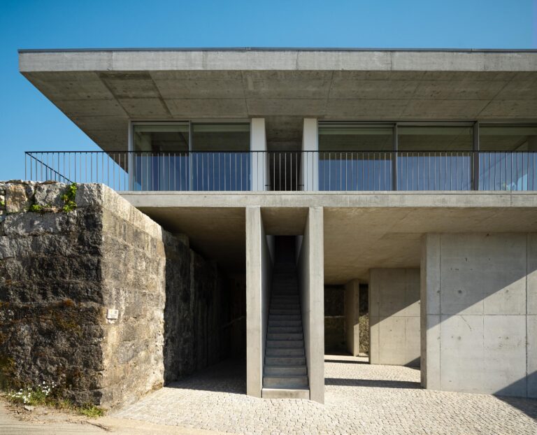 Fachada da moradia em betão aparente, com volume superior em consola, varanda e escadaria de acesso. Pavimento em calçada — CASA COQUEIRA arquitectura Tiago Sousa Arquitecto fotografia Ivo Tavares