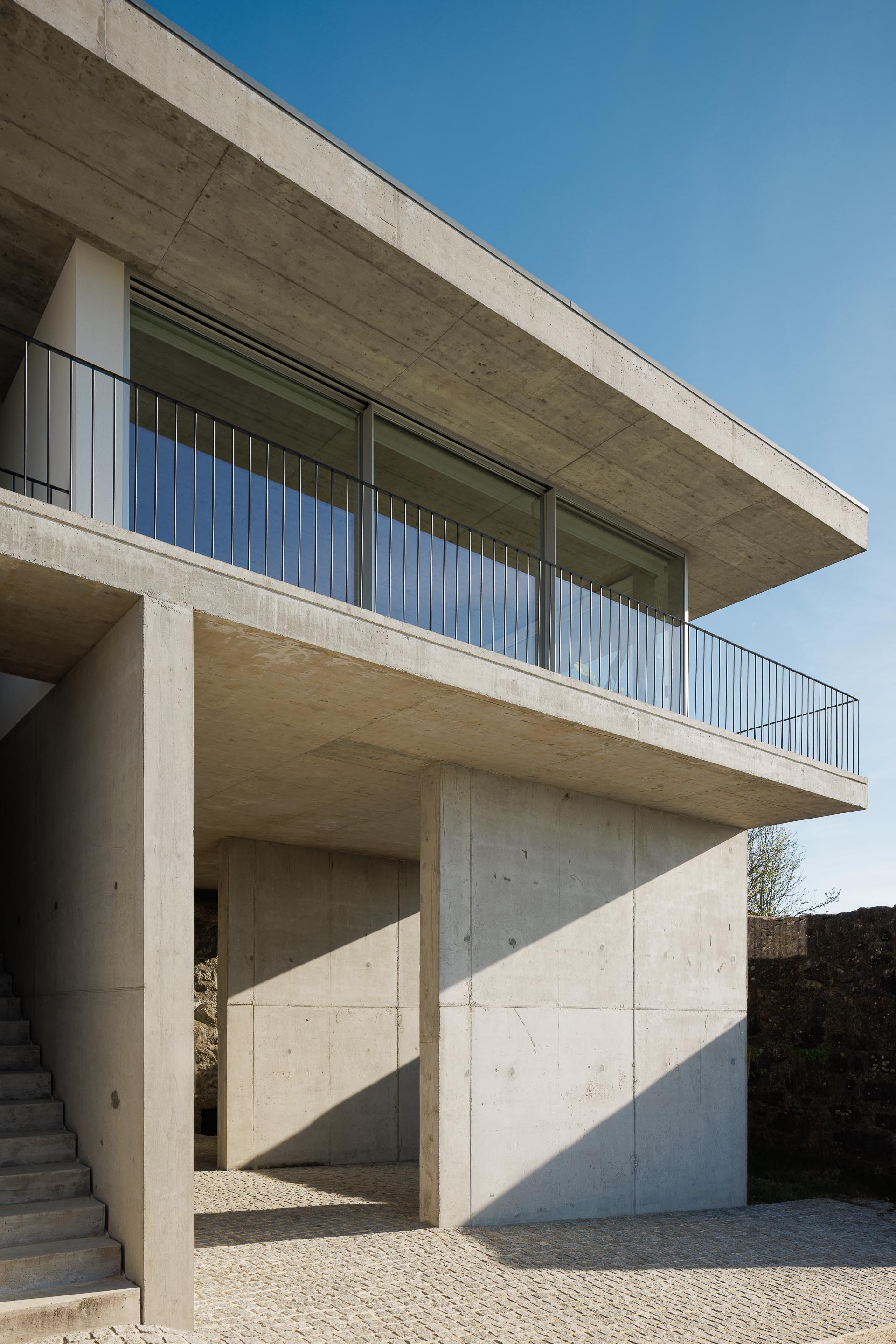 Moradia em betão aparente com varanda e guarda-corpos metálicos, vãos envidraçados e escadaria exterior. Luz e sombra — CASA COQUEIRA arquitectura Tiago Sousa Arquitecto fotografia Ivo Tavares