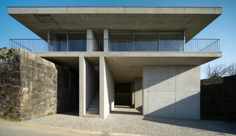 Fachada principal da moradia em betão aparente, com dois pisos, varanda superior e escadaria central. Muro de pedra lateral — CASA COQUEIRA arquitectura Tiago Sousa Arquitecto fotografia Ivo Tavares