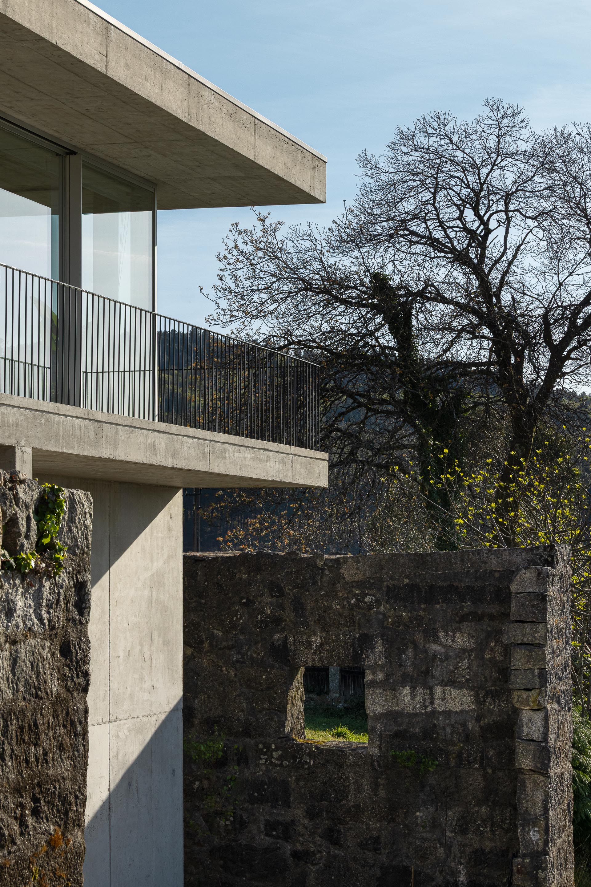 Detalhe da moradia com varanda em betão aparente e guarda-corpos metálicos, adjacente a muro de pedra antigo — CASA COQUEIRA arquitectura Tiago Sousa Arquitecto fotografia Ivo Tavares