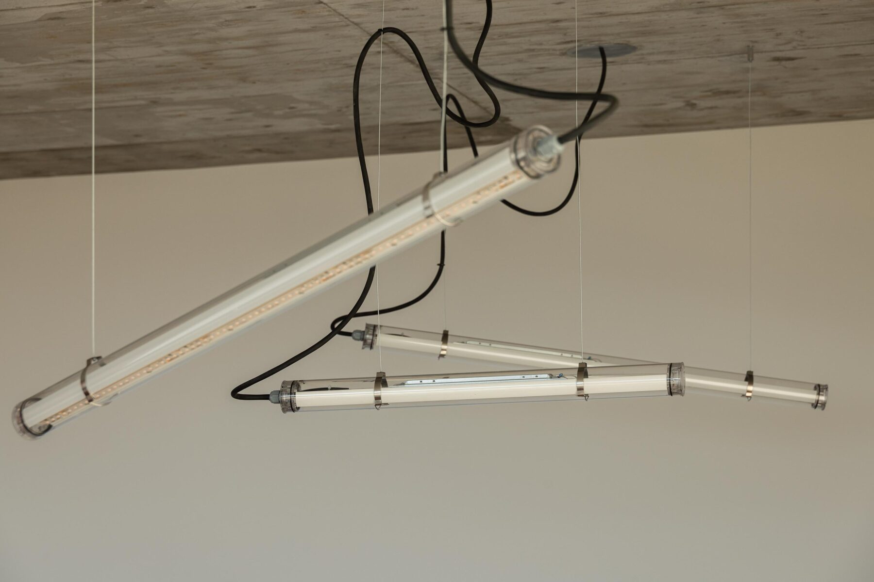Candeeiros tubulares suspensos com cabos pretos, iluminando o teto em betão aparente da área social — CASA COQUEIRA arquitectura Tiago Sousa Arquitecto fotografia Ivo Tavares
