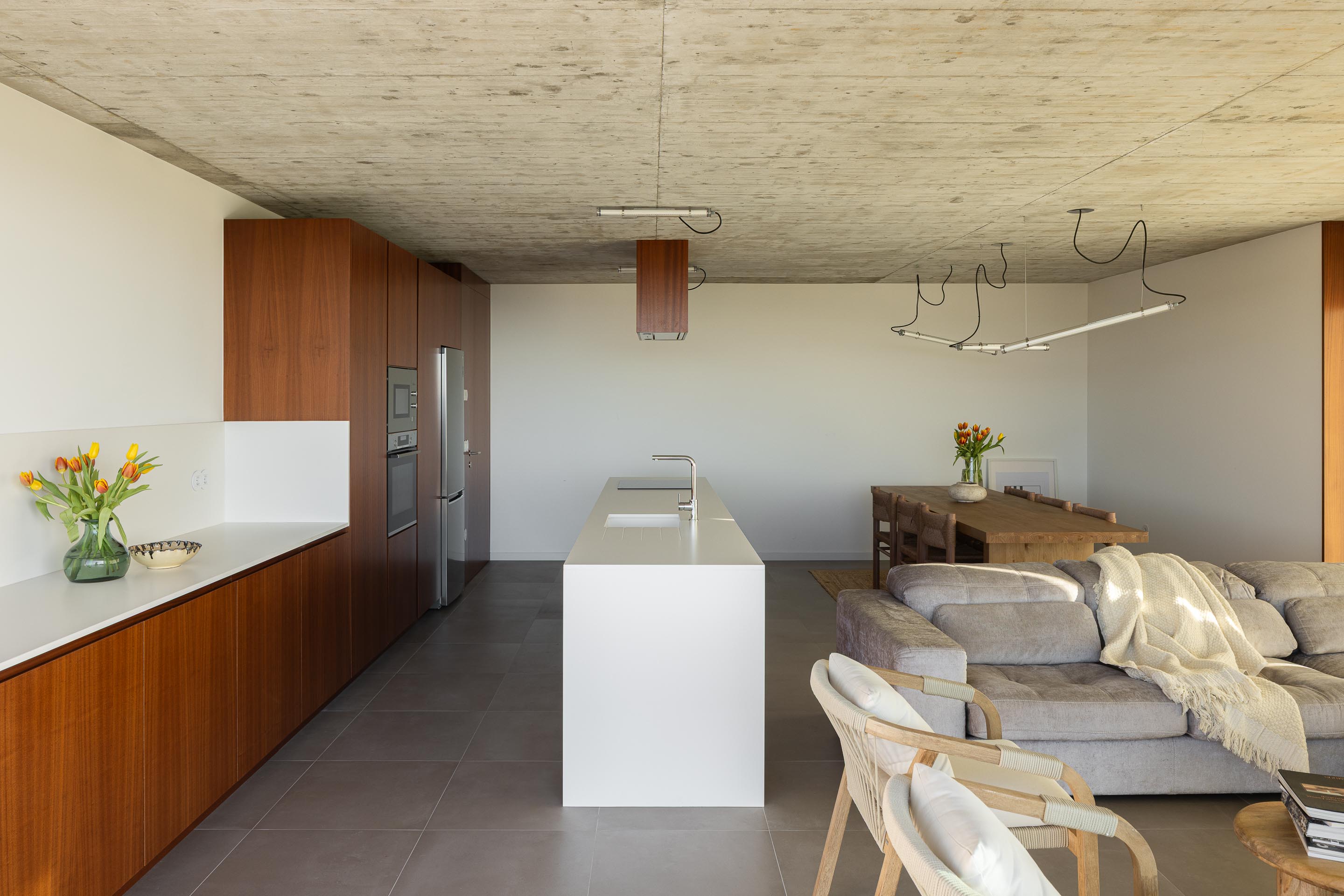 Cozinha e sala de estar em planta aberta, com teto em betão aparente, armários em madeira escura e grandes vãos envidraçados — CASA COQUEIRA arquitectura Tiago Sousa Arquitecto fotografia Ivo Tavares