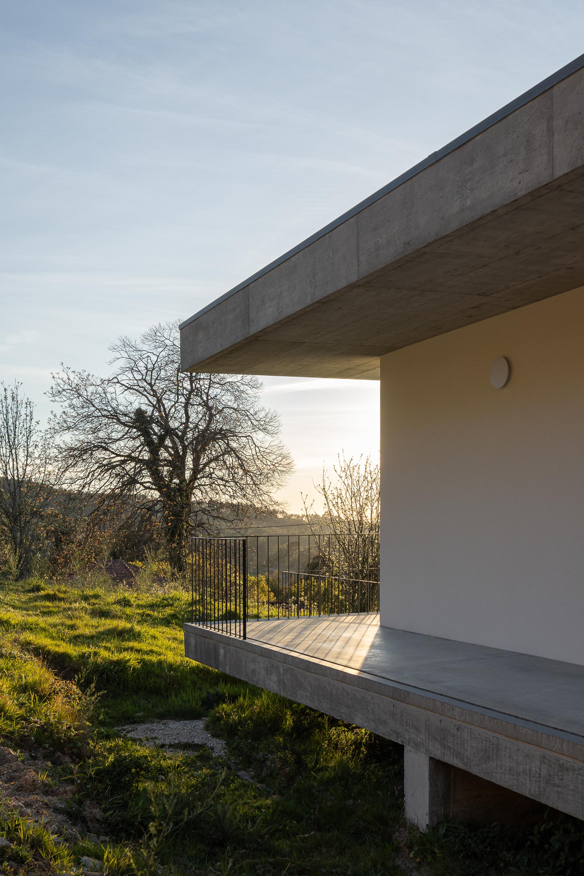 Varanda da moradia em betão aparente com guarda-corpos metálicos, ao pôr do sol, com vista para a paisagem — CASA COQUEIRA arquitectura Tiago Sousa Arquitecto fotografia Ivo Tavares