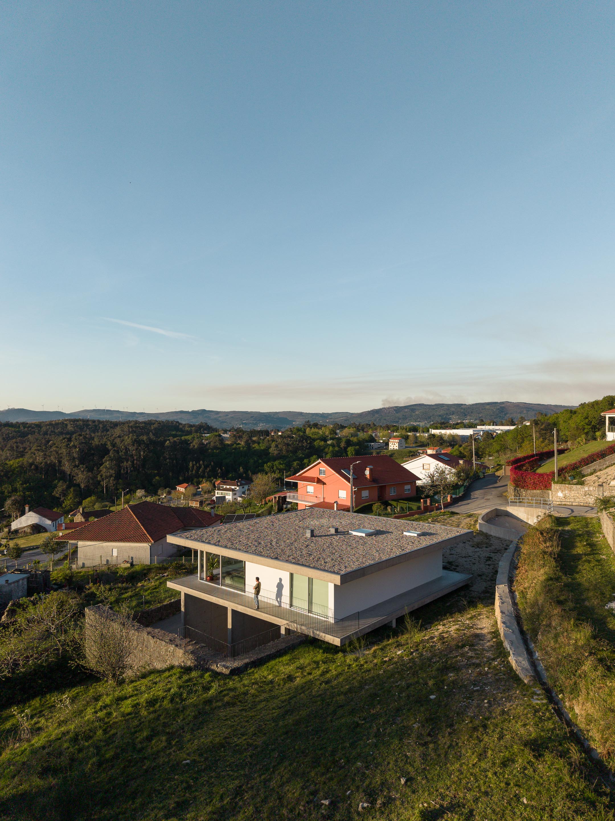 Vista aérea da moradia com cobertura plana e varandas, implantada na encosta, com contexto rural e montanhoso — CASA COQUEIRA arquitectura Tiago Sousa Arquitecto fotografia Ivo Tavares