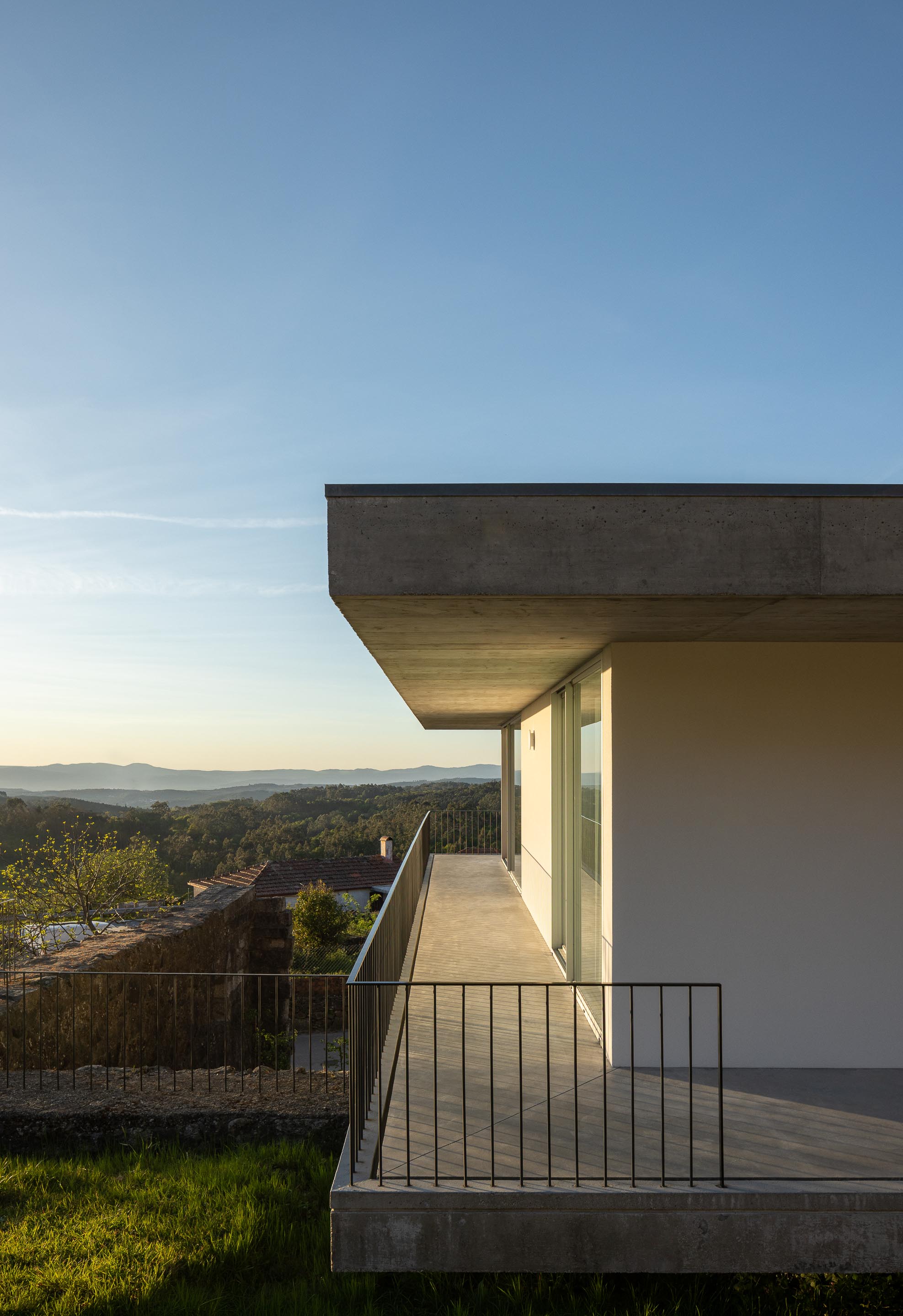 Varanda em betão aparente com guarda-corpos metálicos, estendendo-se da moradia, com vista panorâmica da paisagem — CASA COQUEIRA arquitectura Tiago Sousa Arquitecto fotografia Ivo Tavares
