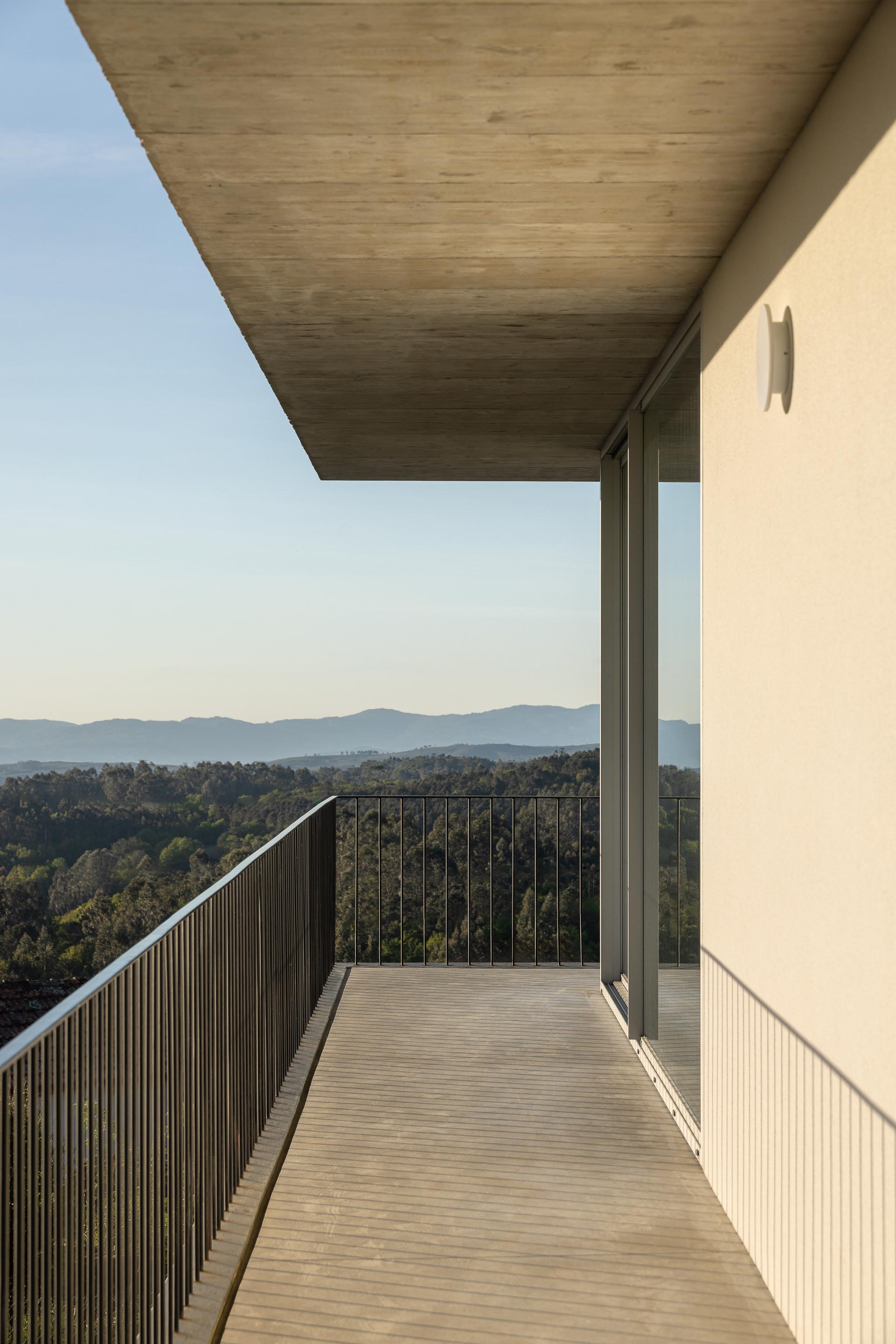 Varanda da moradia em betão aparente com guarda-corpos metálicos, ladeada por fachada branca e grandes vãos envidraçados — CASA COQUEIRA arquitectura Tiago Sousa Arquitecto fotografia Ivo Tavares