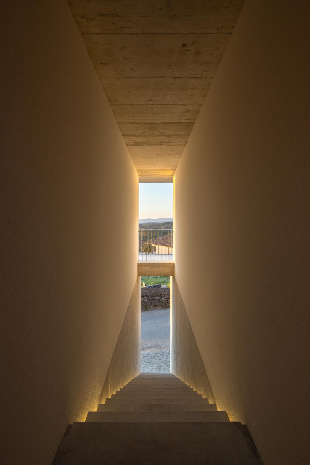 Escadaria interior de betão aparente, iluminada por luz linear, conduzindo a um vão com vista para o exterior — CASA COQUEIRA arquitectura Tiago Sousa Arquitecto fotografia Ivo Tavares