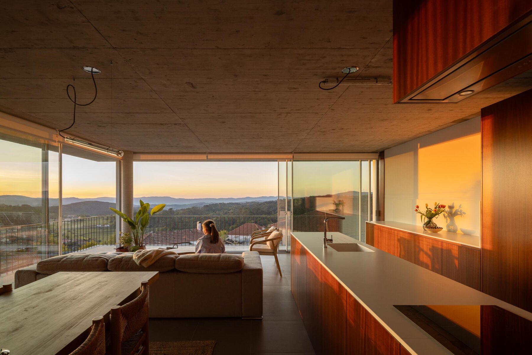 Sala de estar e cozinha em planta aberta, com vista panorâmica através de grandes vãos envidraçados ao pôr do sol — CASA COQUEIRA arquitectura Tiago Sousa Arquitecto fotografia Ivo Tavares